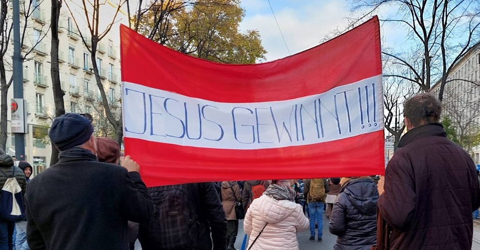 Menschen marschieren auf der Demonstration. Ein Grüppchen trägt eine Österreich-Fahne. Auf ihr die Worte: Jesus gewinnt!!!