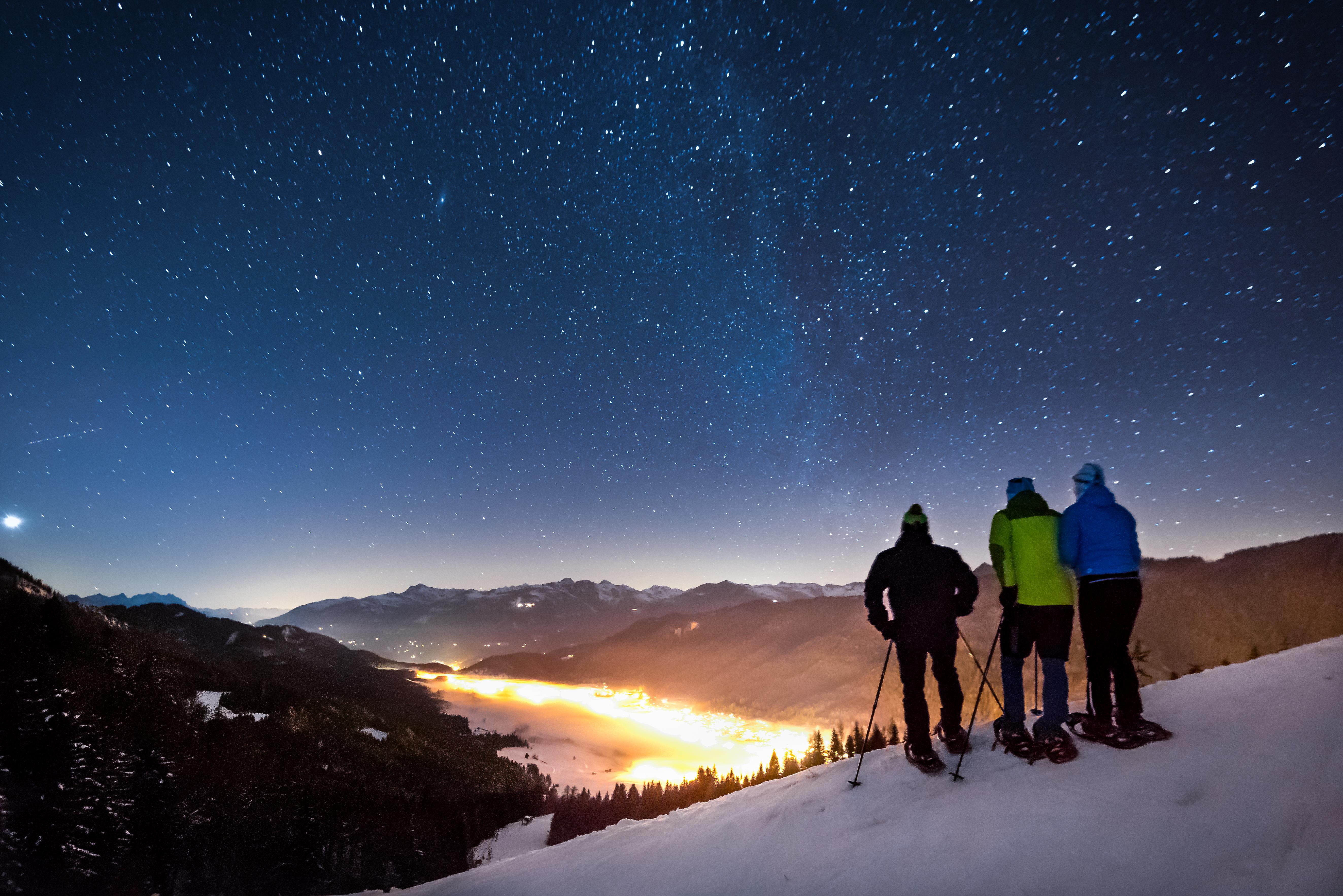 Drei Winterwanderer blicken in einen von unzähligen Sternen hell erleuchteten Nachthimmel