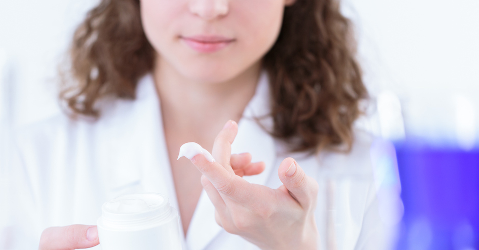 Eine junge Frau im weißen Kittel hat mit dem Finger Creme aus einem Tiegel entnommen