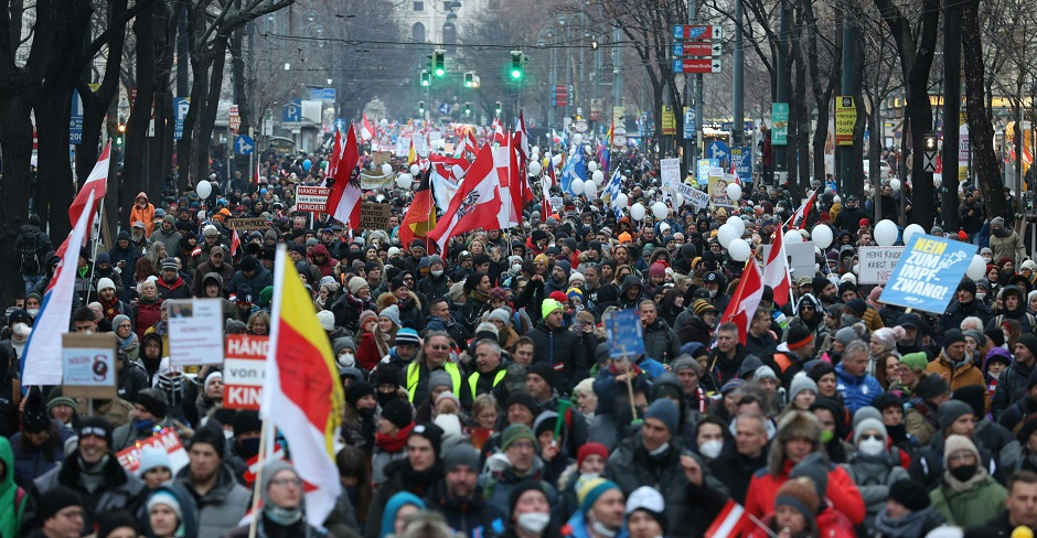 Tausende Menschen protestieren auf dem Wiener Ring. Eine Straße mit Menschenmassen. Sie schwenken Fahnen und halten Schilder.