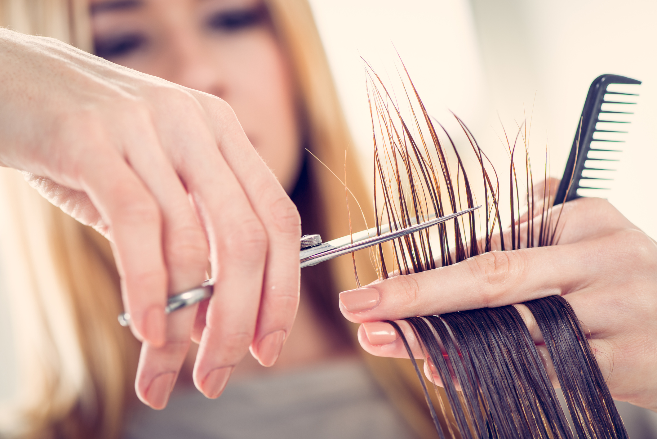Eine Friseurin unscharf im Hintergrund, im Vordergrund ihre Hände beim Schneiden