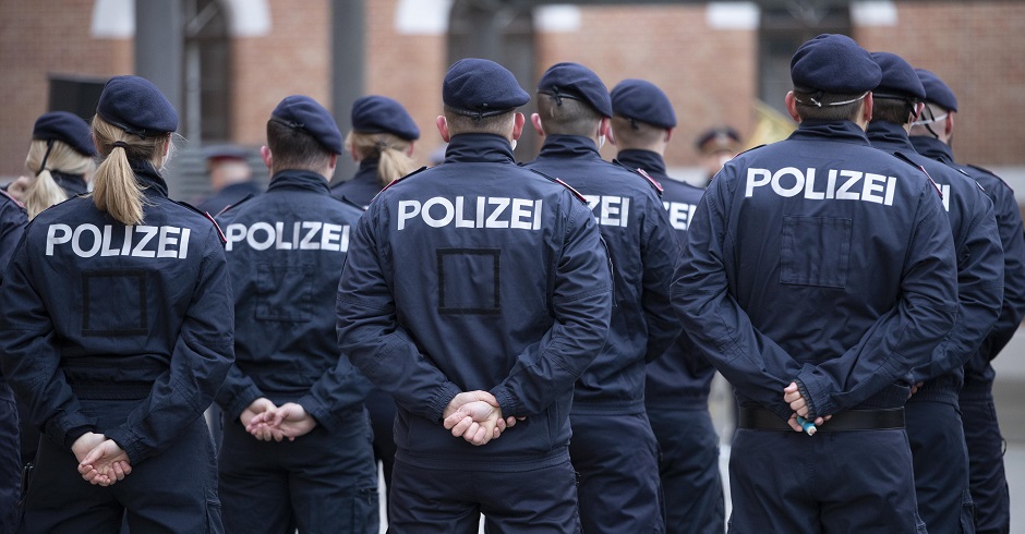 Eine Gruppe Polizisten in Uniform von hinten. Sie haben die Hände hinter dem Rücken verschränkt.