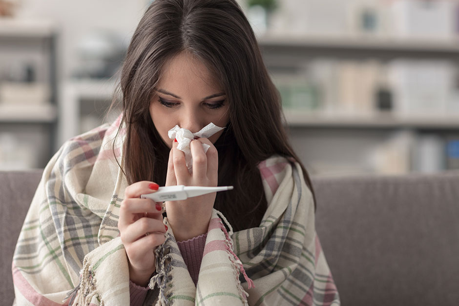 Eine in Decken gehüllte, erkältete Frau putzt sich die Nase | Credit: iStock.com/cyano66