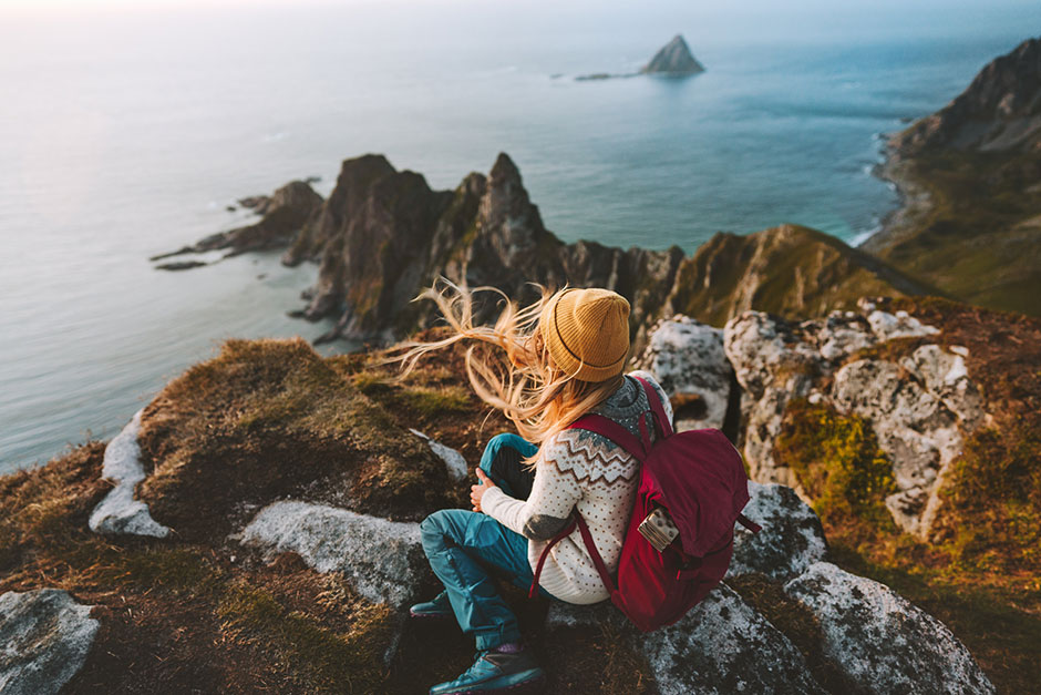Rucksacktouristin sitzt auf einem Felsen mit Blick auf das offene Meer | Credit: iStock.com/Everste
