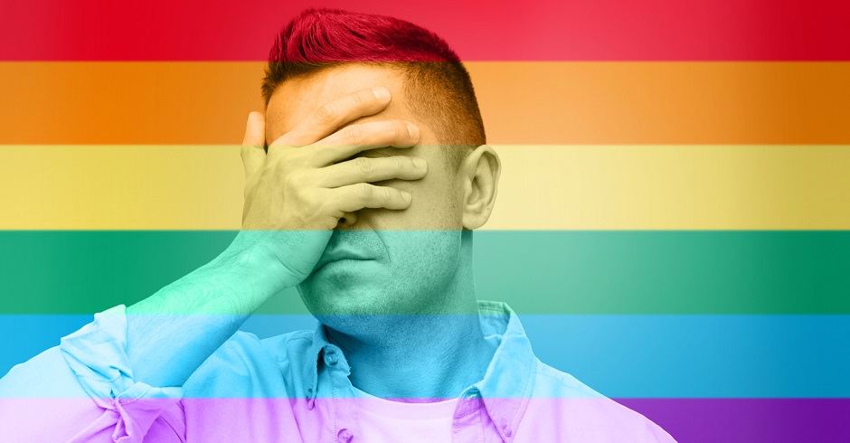 Ein Mann hält sich verzweifelt die Hand vor das Gesicht. Das Bild ist in den Farben der Regenbogenflagge gefärbt, ein Symbol für die LGBT-Community