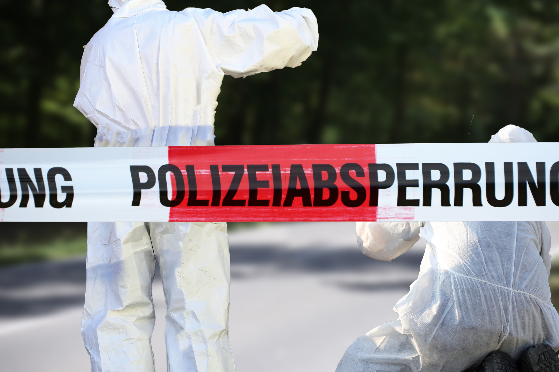 Zwei Mitarbeiter der Spurensicherung in weißen Overalls hinter einer Polizeiabsperrung