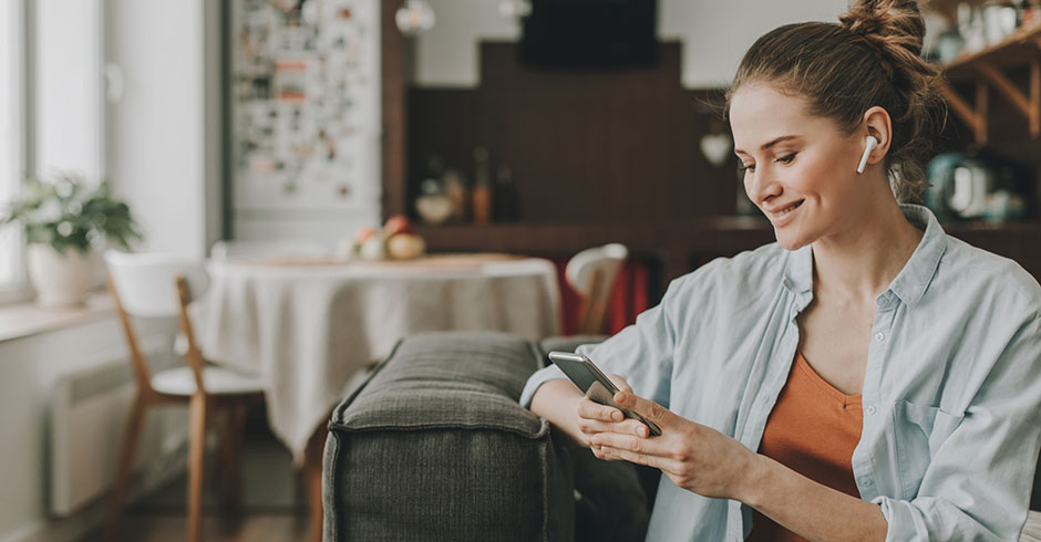 Junge Studentin tippt auf ihrer Couch Nachrichten auf ihrem Smartphone | Credit: iStock.com/YakobchukOlena