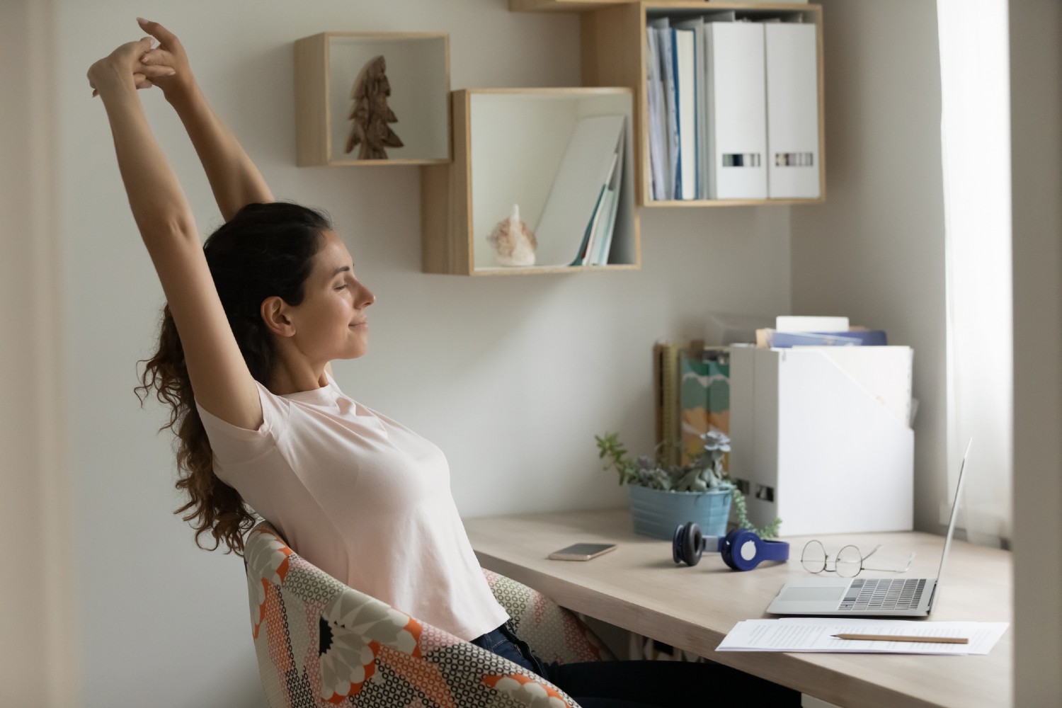 Frau sitzt vor Schreibtisch und streckt sich | Credit: iStock.com/fizkes