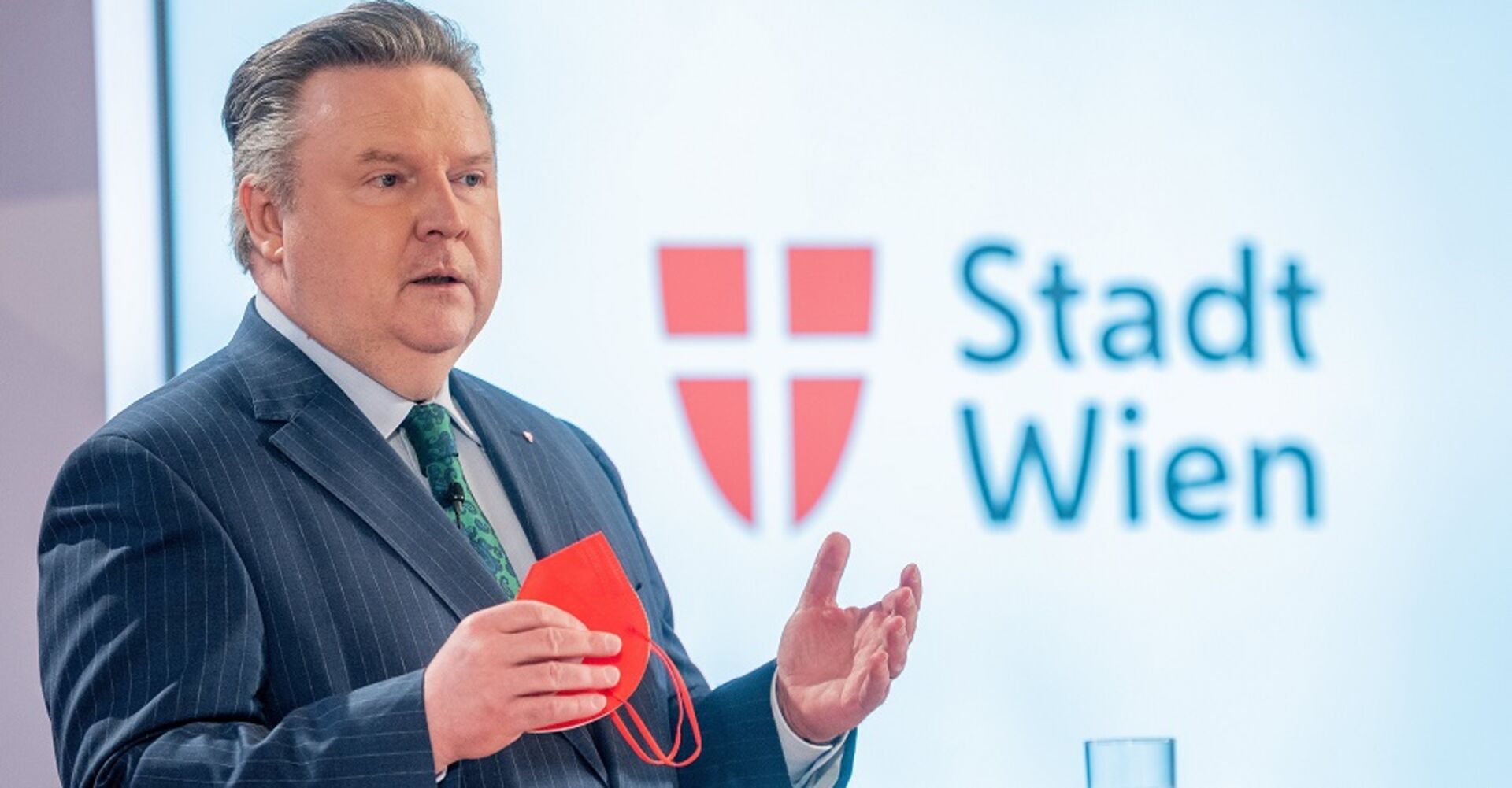 Bürgermeister Michael Ludwig erklärt auf einer Pressekonferenz die aktuelle Situation. Er hält eine rote FFP2-Maske in der Hand. Im Hintergrund der Schriftzug "Stadt Wien", daneben das Wiener Stadtwappen.