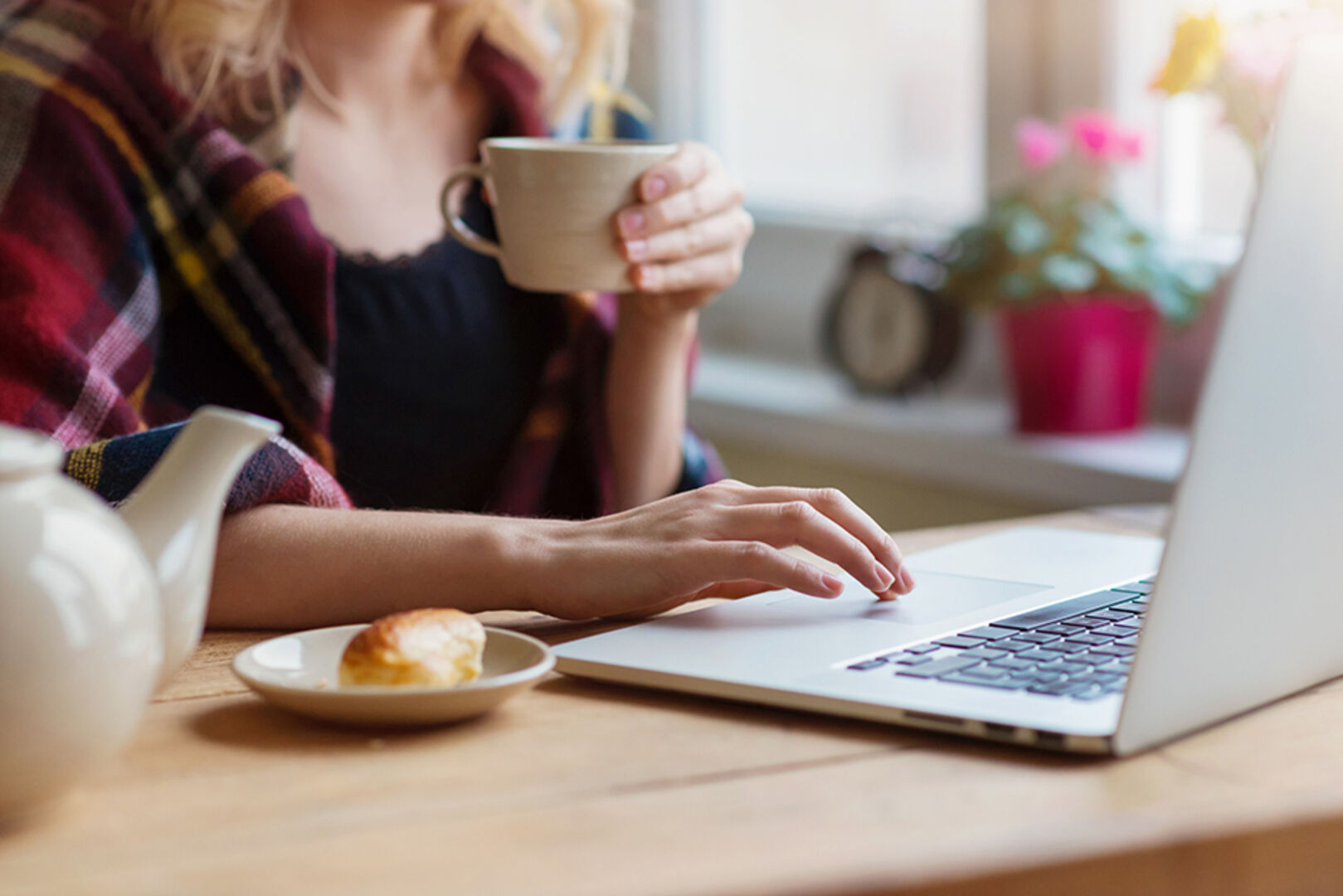 Junge Frau trinkt während der Arbeit am Notebook eine Tasse Kaffee | Credit: iStock.com/Halfpoint