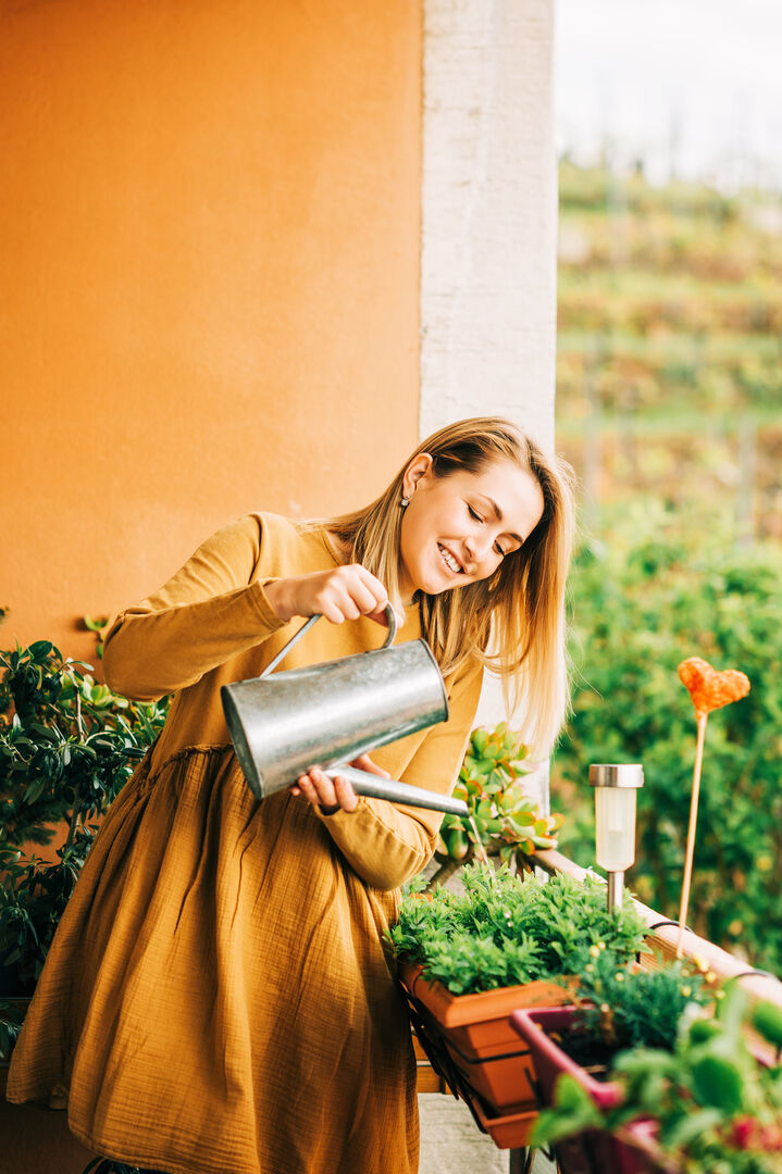 Frau im orangen Kleid gießt Pflanzen | Credit: iStock.com/Anna Nahabed