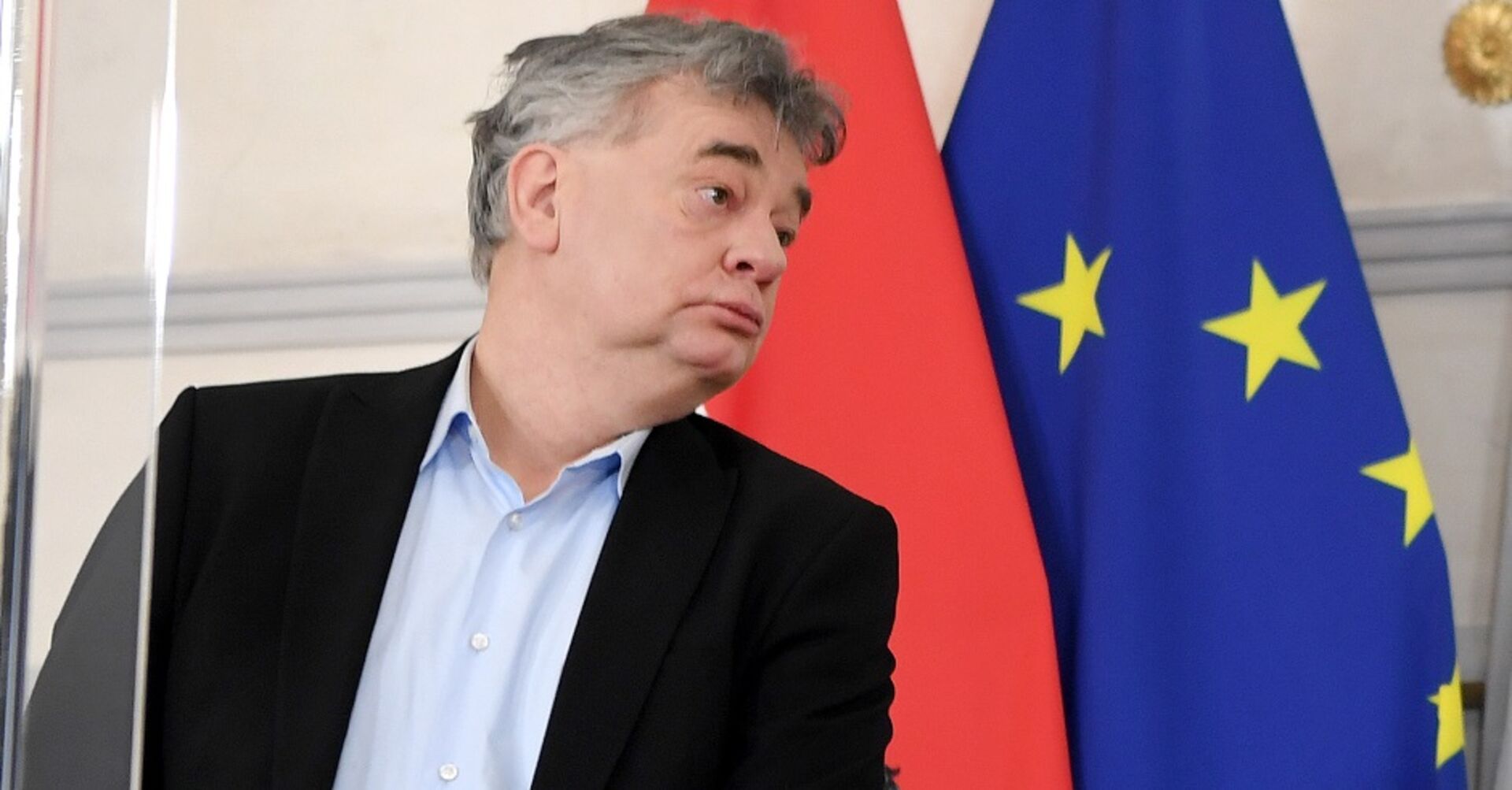 Vizekanzler Werner Kogler im Halbprofil nach rechts schauend beim Pressefoyer. Im Hintergrund die österreichische und die EU-Flagge