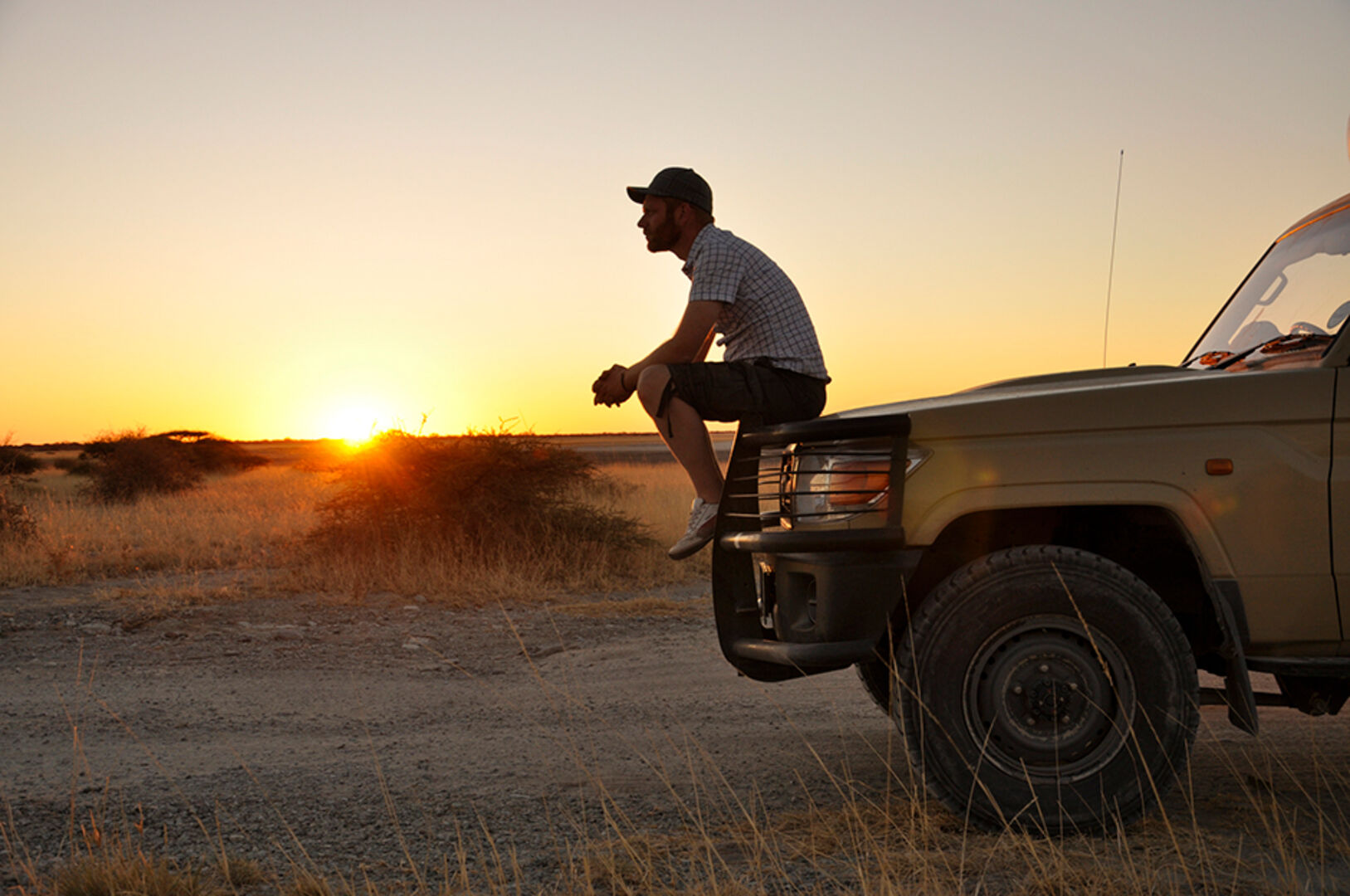 Mann sitzt auf der Front seines Autos und genießt den Sonnenuntergang | Credit: iStock.com/trulli