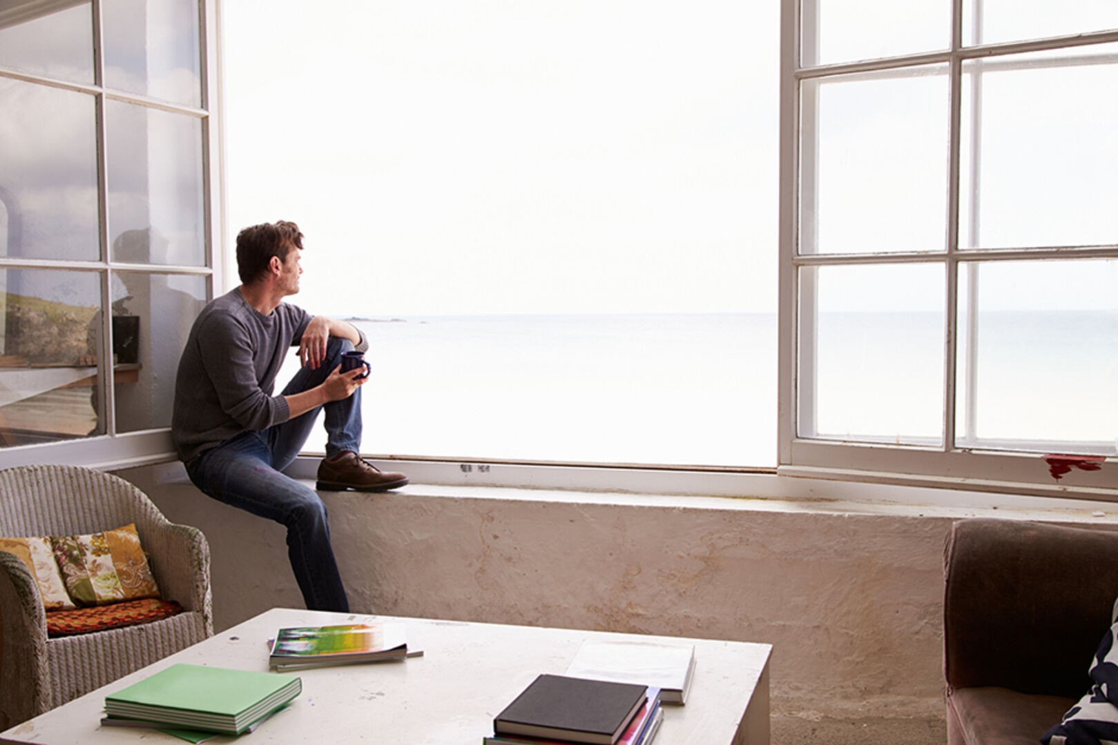 Mann sitzt nachdenklich am offenen Fenster | Credit: iStock.com/monkeybusinessimages