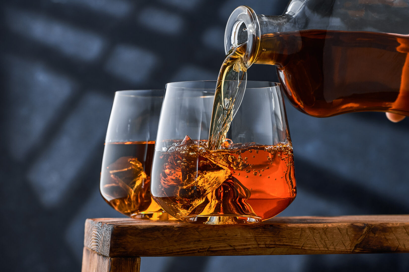 Zwei elegante Gläser Whiskey stehen auf einem Tisch, das sich im Vordergrund befindende wird aus einer Flasche befüllt