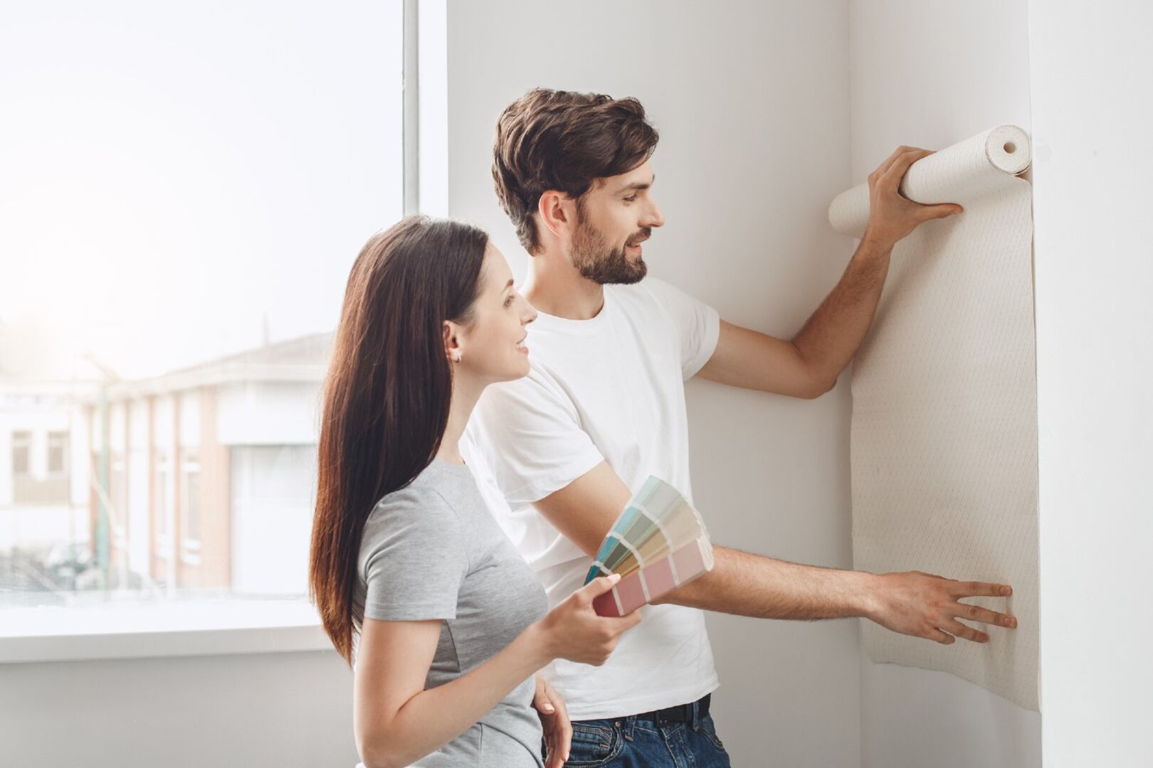 Mann und Frau stehen mit Tapetenrolle vor einer Wand | Credit: iStock.com/dima_sidelnikov