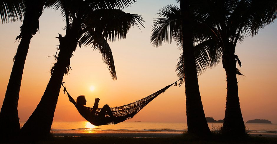 Junge Frau beim Lesen in der Hängematte an einem Strand bei Sonnenuntergang | Credit: iStock.com/anyaberkut