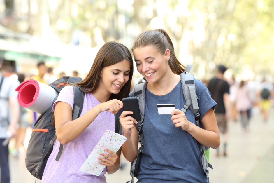 Zwei junge Rucksack-Touristinnen surfen via Smartphone nach Reiseinformationen | Credit: iStock.com/AntonioGuillem