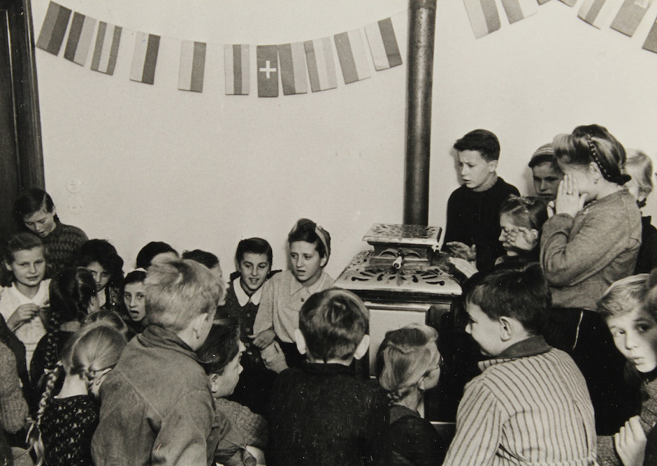 Schwarzweiß Aufnahme, Kinder versammeln sich um Ofen