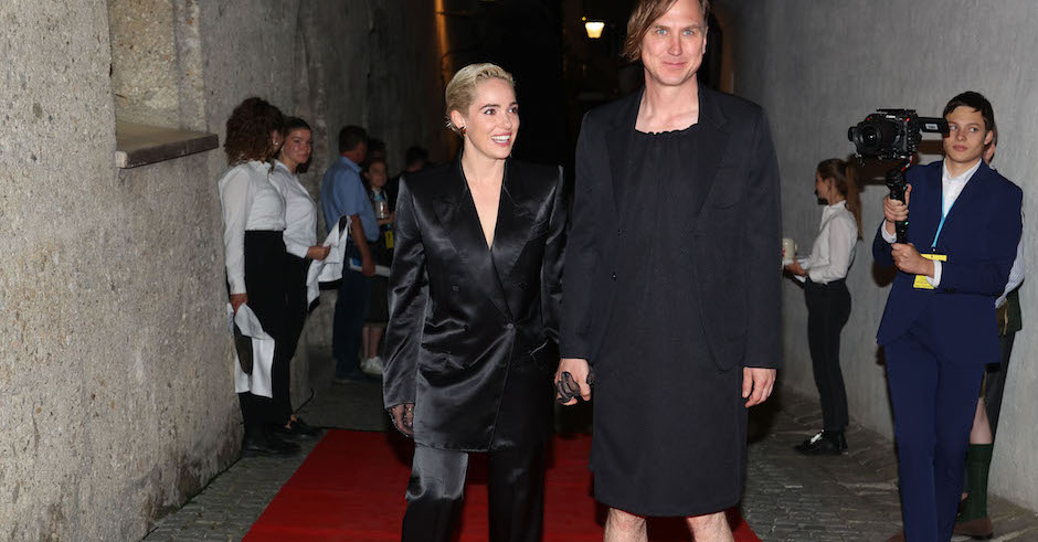Verena Altenberger und Lars Eidinger händchenhaltend bei der Premierenfeier am roten Teppich. Eidinger trägt ein schwarzes Kleid