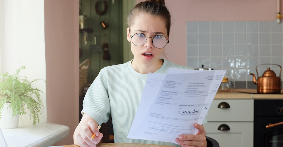 Frau im hellen Pullover schaut geschockt auf Rechnung | Credit: iStock.com/Damir Khabirov