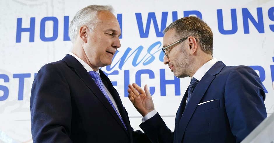 Walter Rosenkranz und Herbert Kickl im Gespräch vor einer Wand mit dem Schriftzug: "Holen wir uns Österreich zurück"