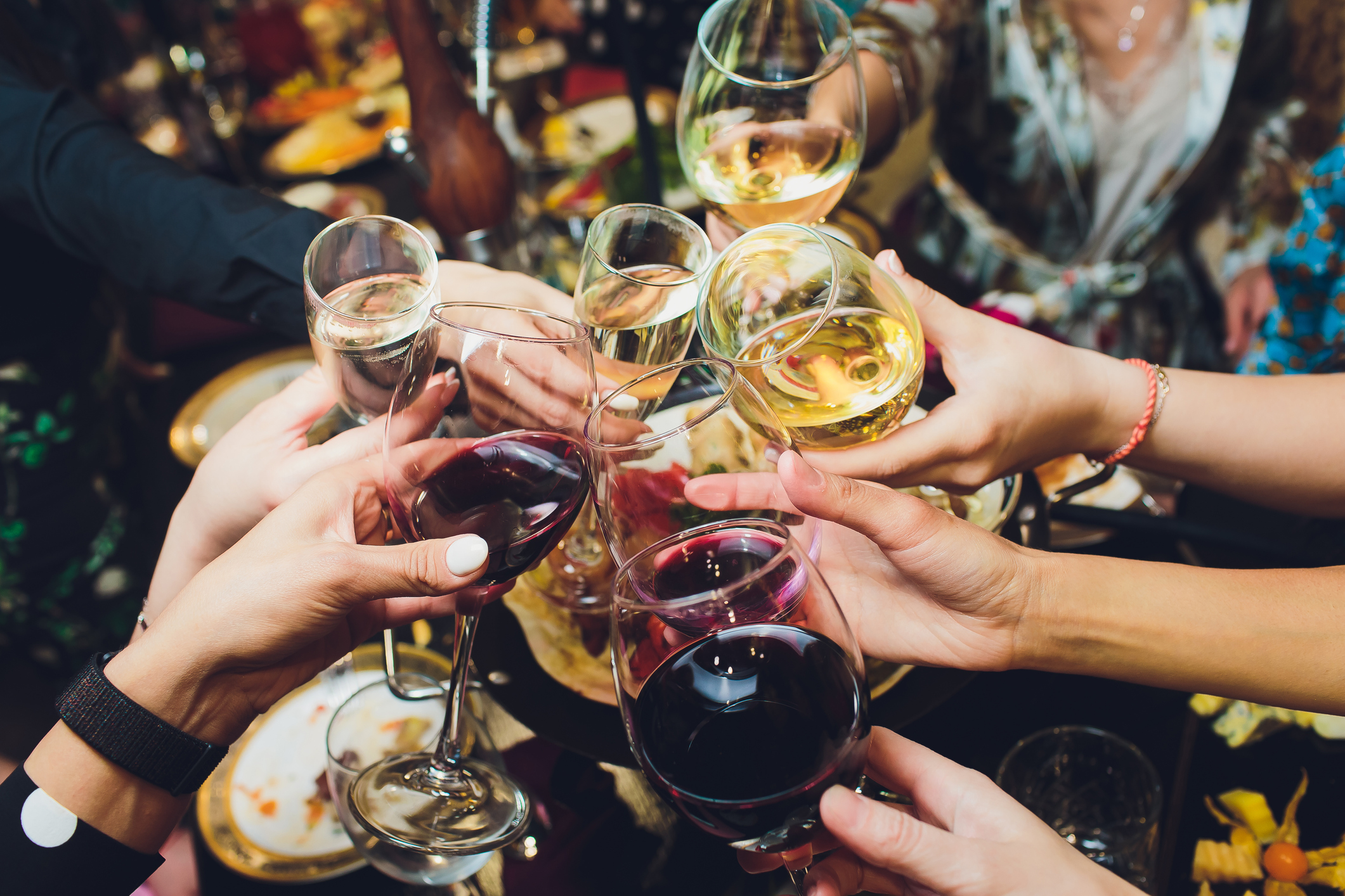 Mehrere Hände, die mit Wein- und Sektgläsern anstoßen.