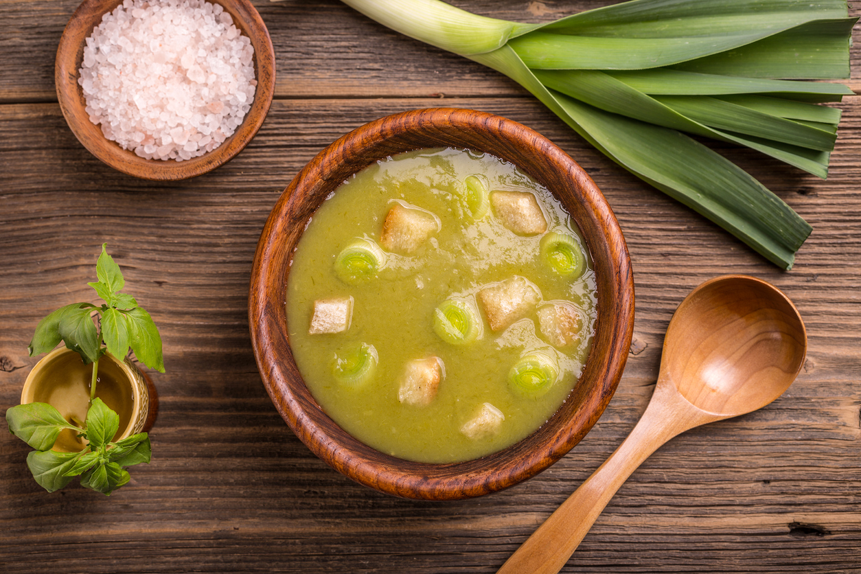 Eine Vichyssoise in einer Holzschale auf einem Tisch mit Meersalz und einem Bund Lauch