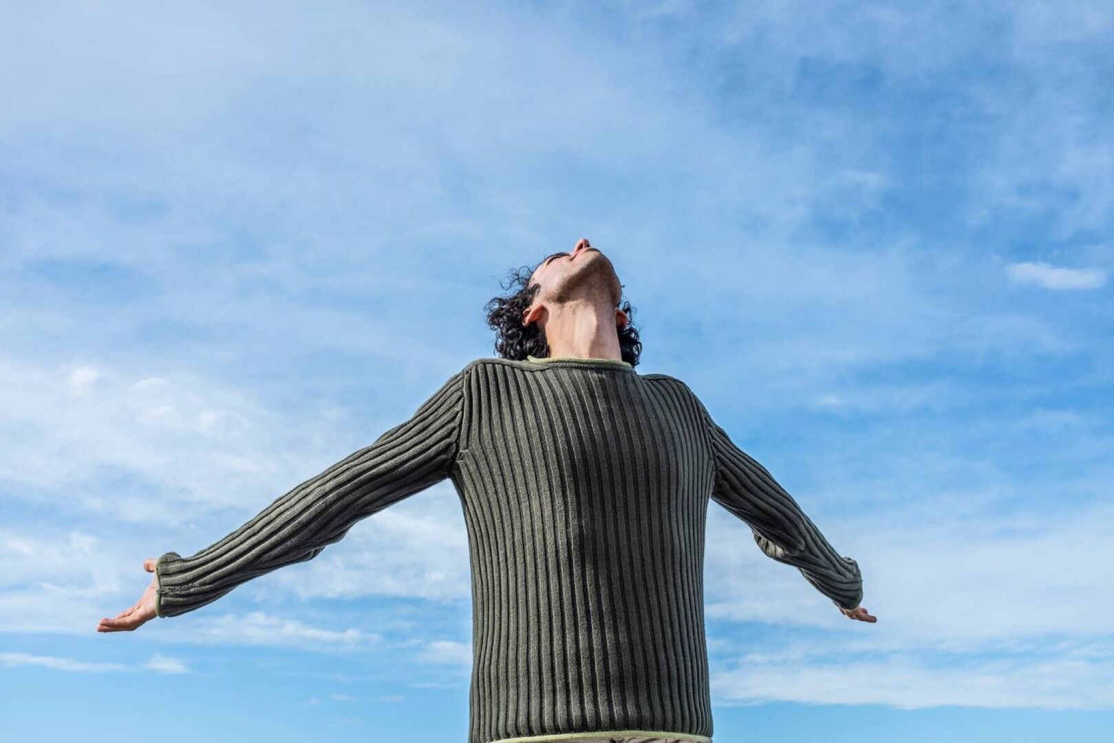 Junger Mann streckt die Arme seitlich weit von sich und legt dabei den Kopf in den Nacken | Credit: iStock.com/luana rigolli