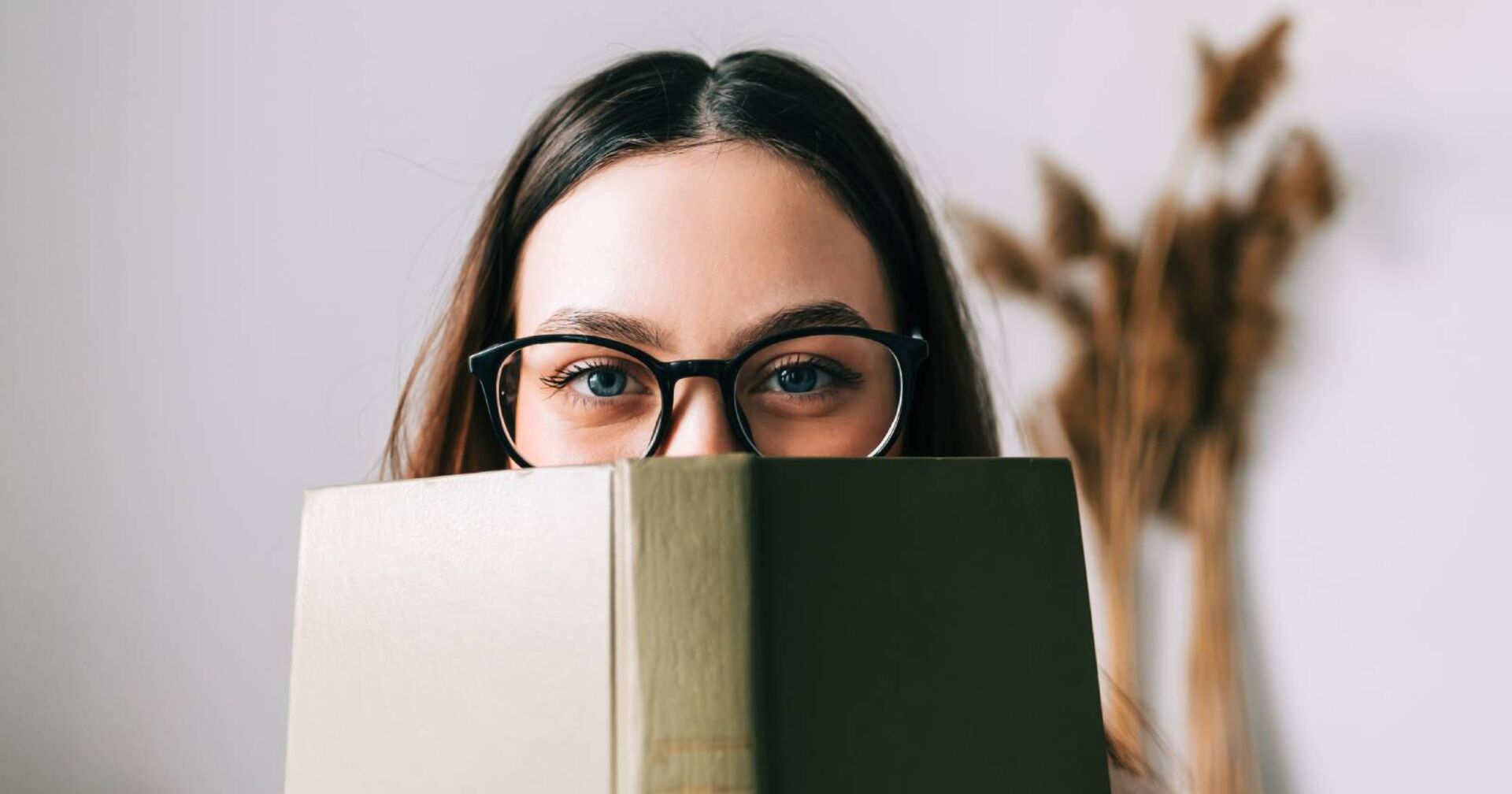 Junge Studentin verbirgt ihr Gesicht hinter einem Buch | Credit: iStock.com/nikkimeel