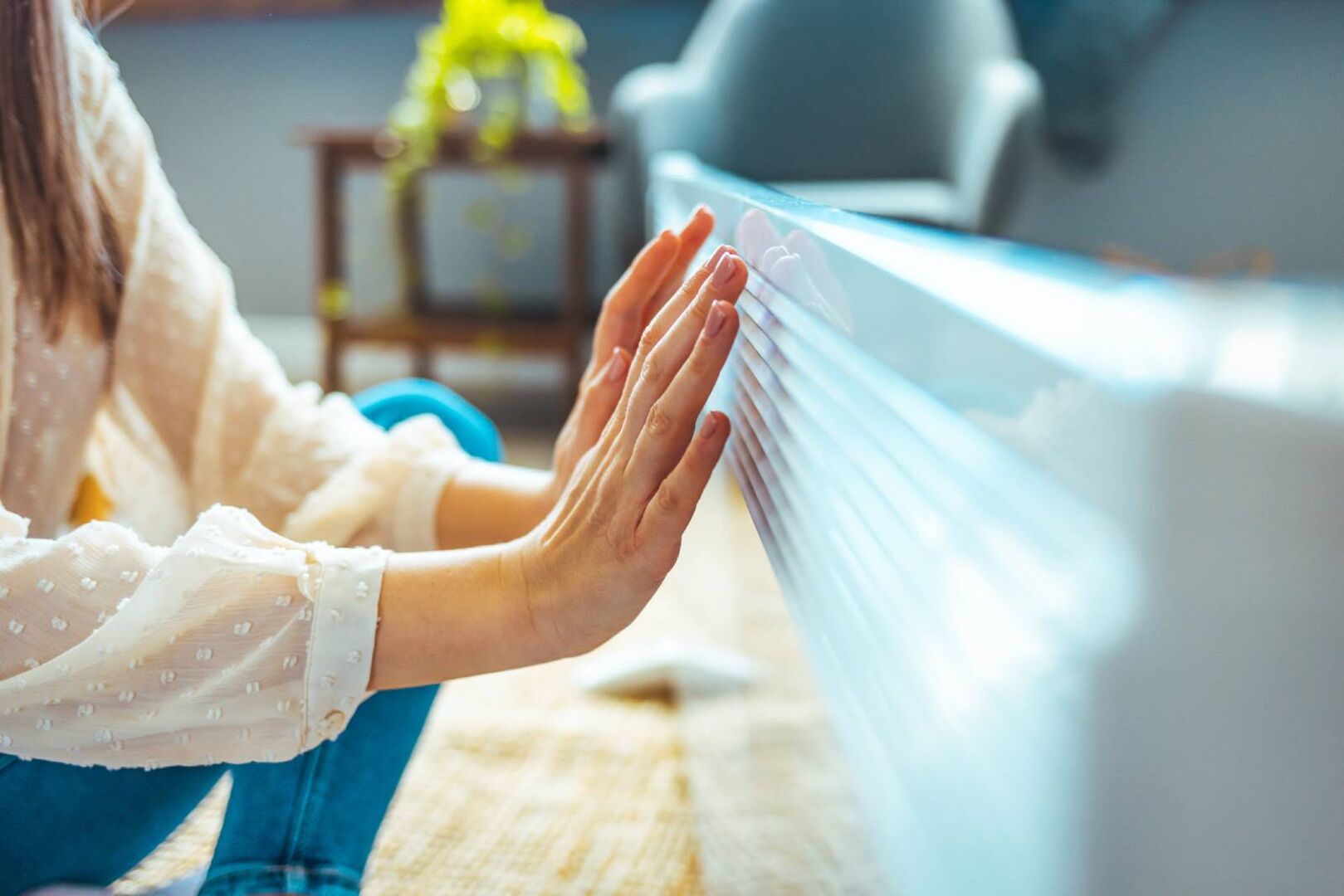 Junge Frau wärmt ihre Hände an der Heizung | Credit: iStock.com/dragana991