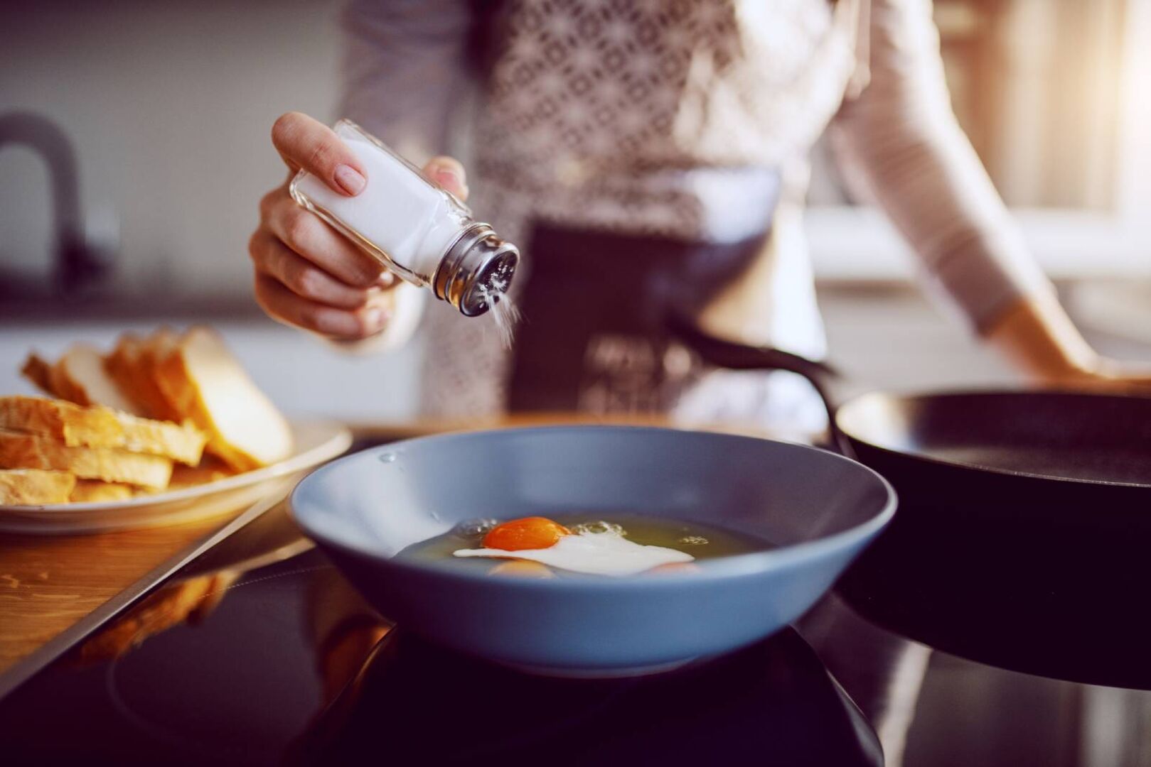 Junge Frau salzt ihr Spiegelei in der Pfanne | Credit: iStock.com/dusanpetkovic