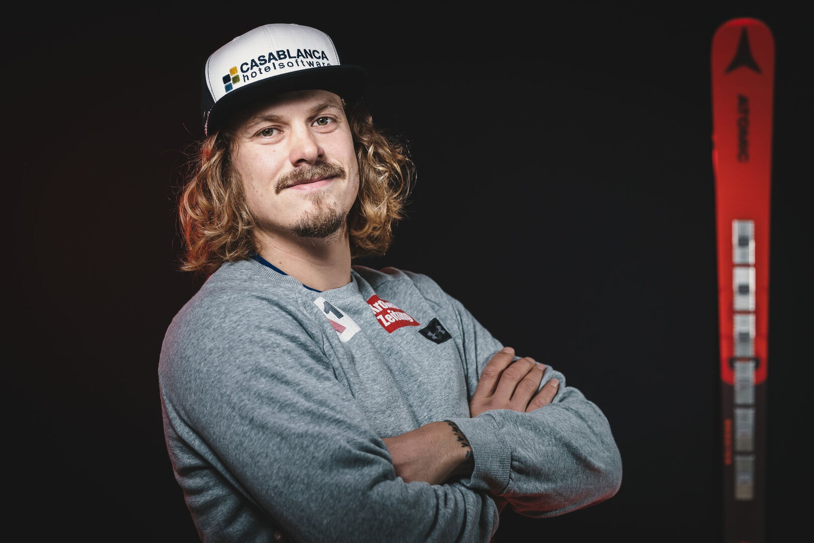 Manuel Feller, der mit verschränkten Armen und einer Baseballmütze auf dem Kopf vor seinen Rennski steht.