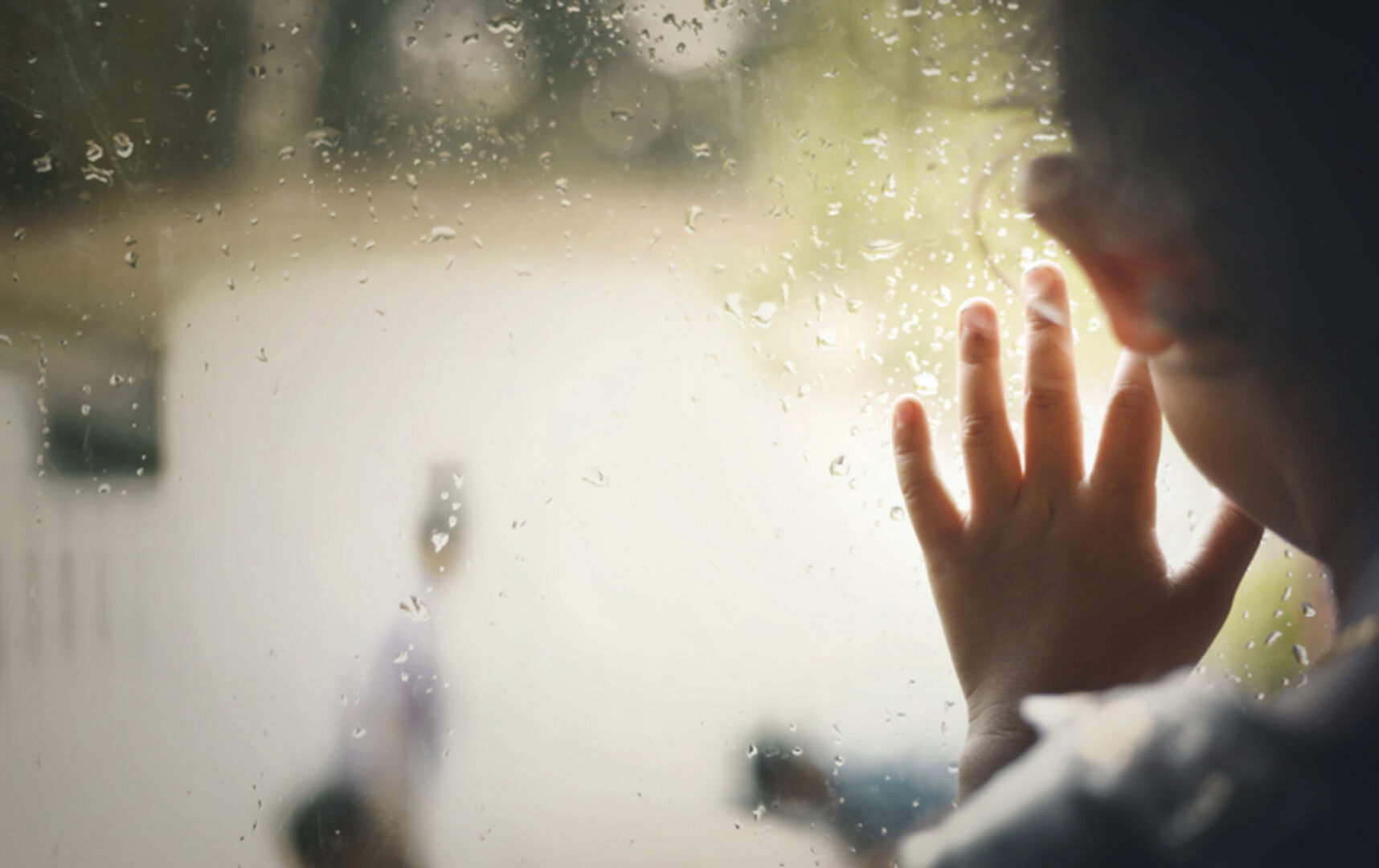 Kind hat Hand am Fenster und schaut raus