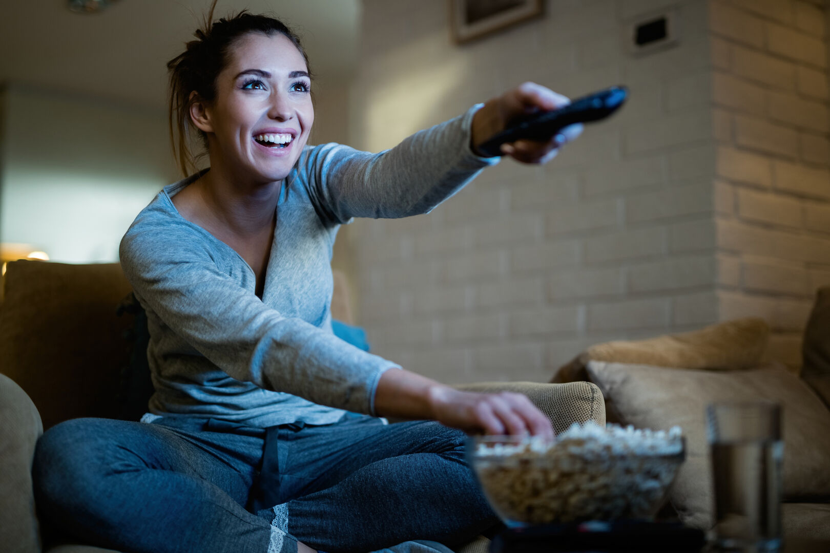 Frau schaltet mit Fernbedienung Fernseher ein