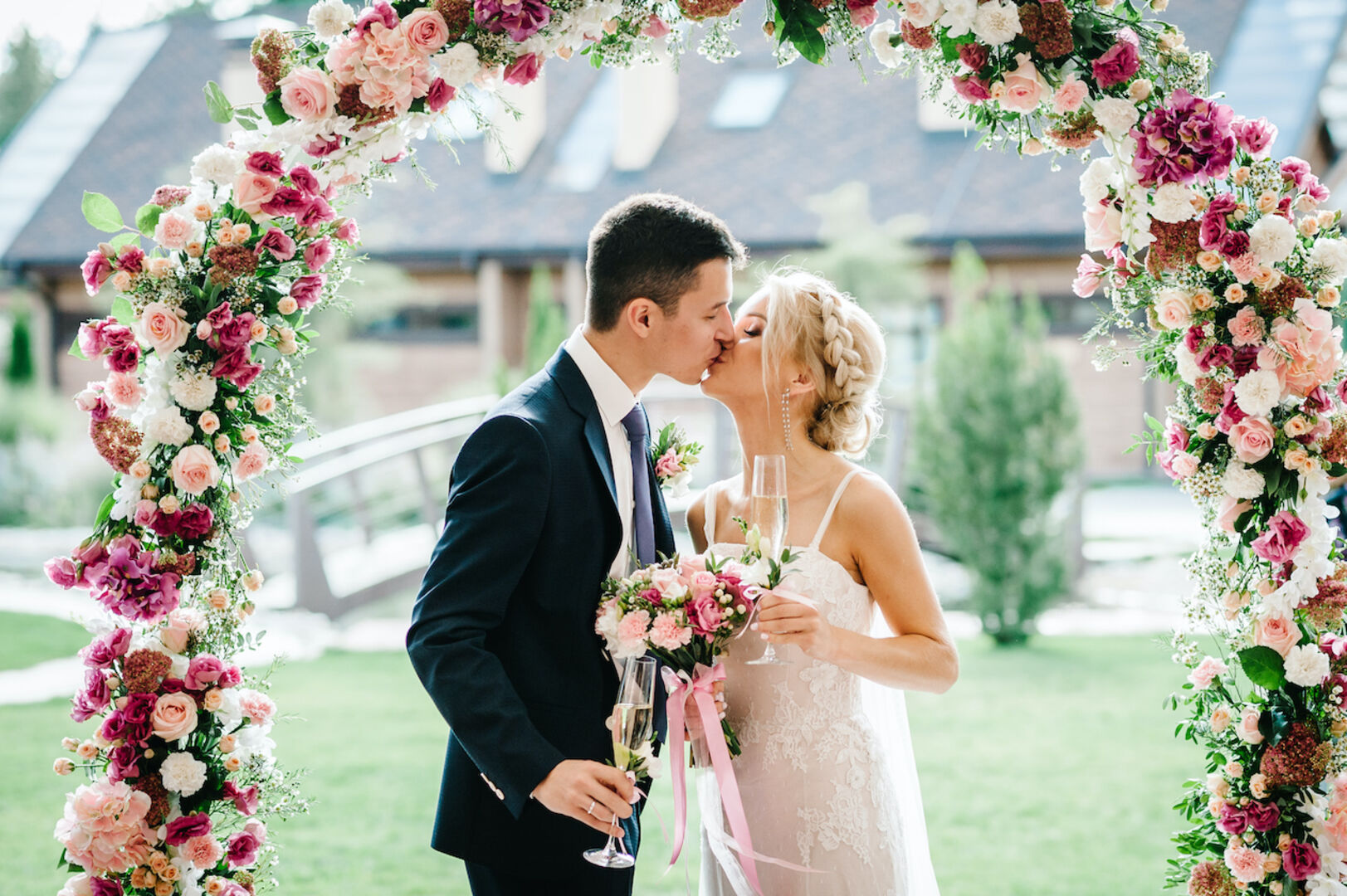 Ein Brautpaar beim Hochzeitskuss unter einem Blumenbogen