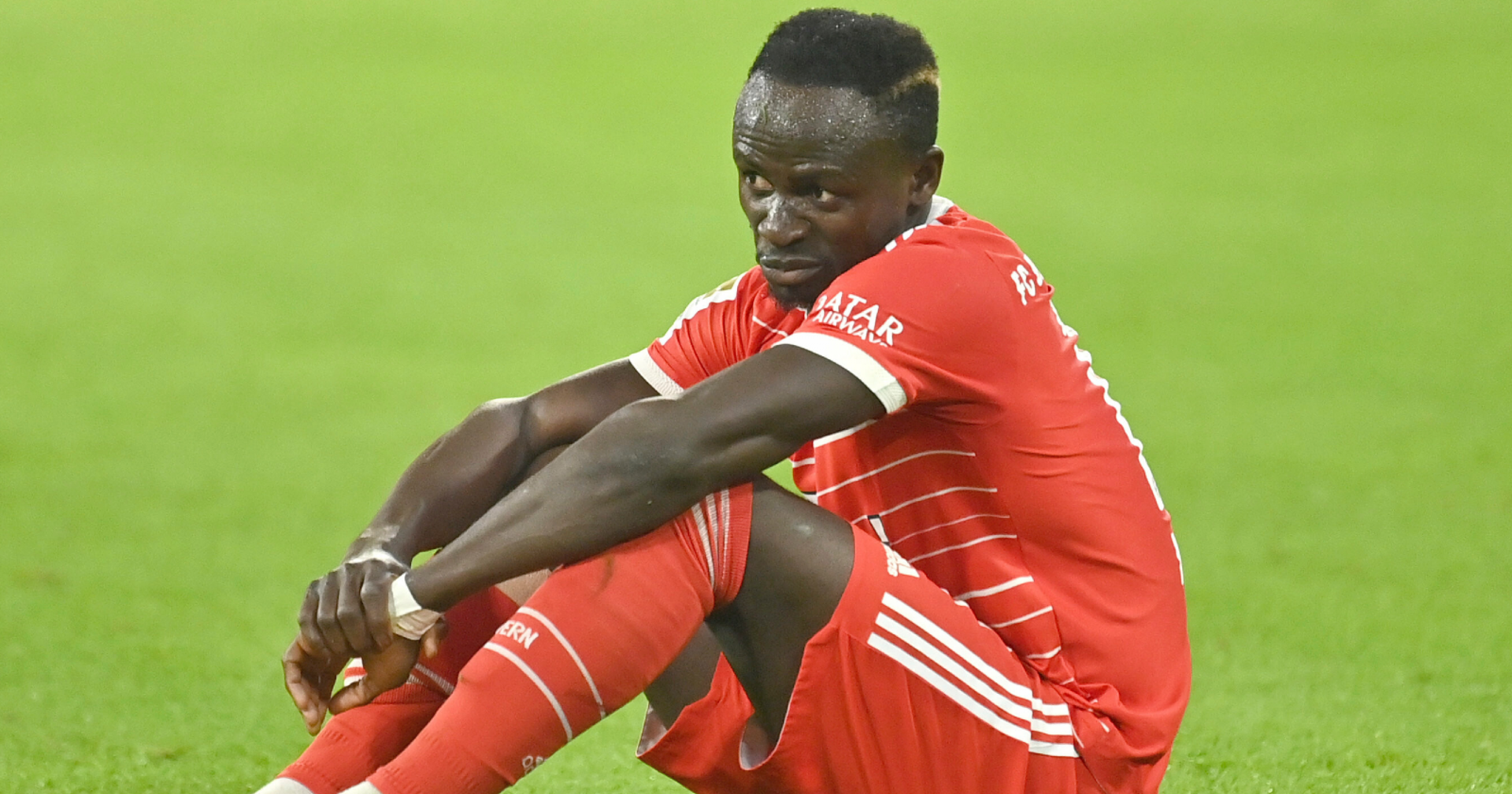 Sadio Mané, der im Dress des FC Bayern München mit einem nachdenklichen Gesichtsausdruck auf dem Spielfeld sitzt.