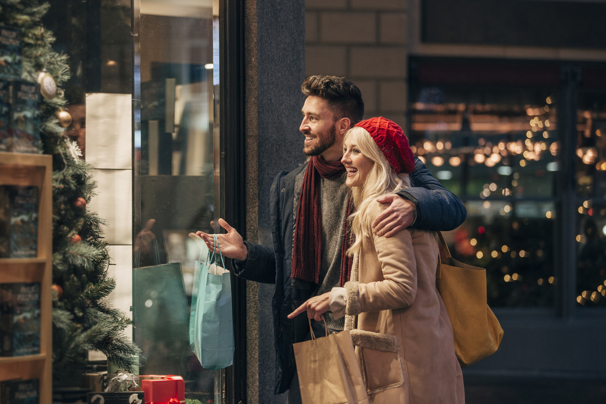 Ein junges Paar, das vor einem weihnachtlich geschmückten Schaufenster steht.