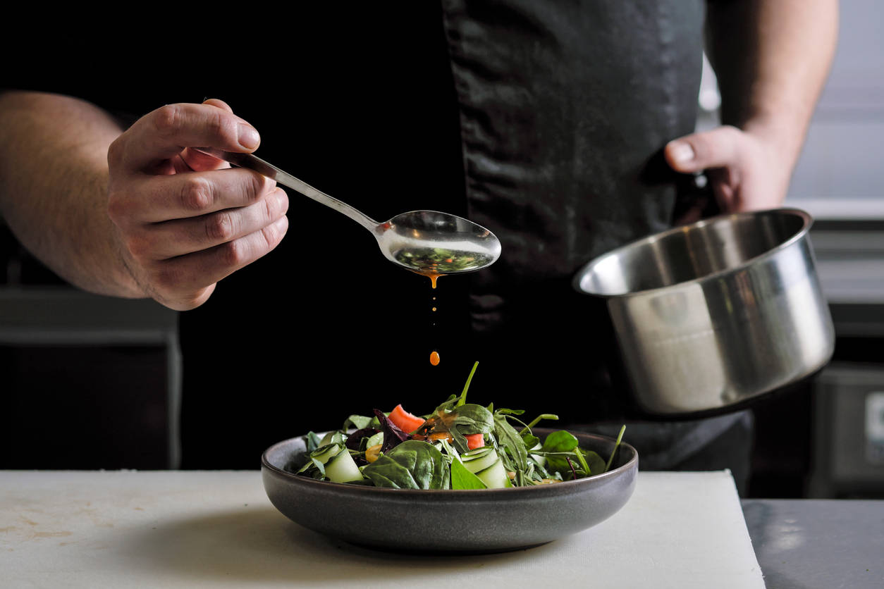Nahaufnahme eines Küchenchefs, der Soße auf eine Salatschale gießt