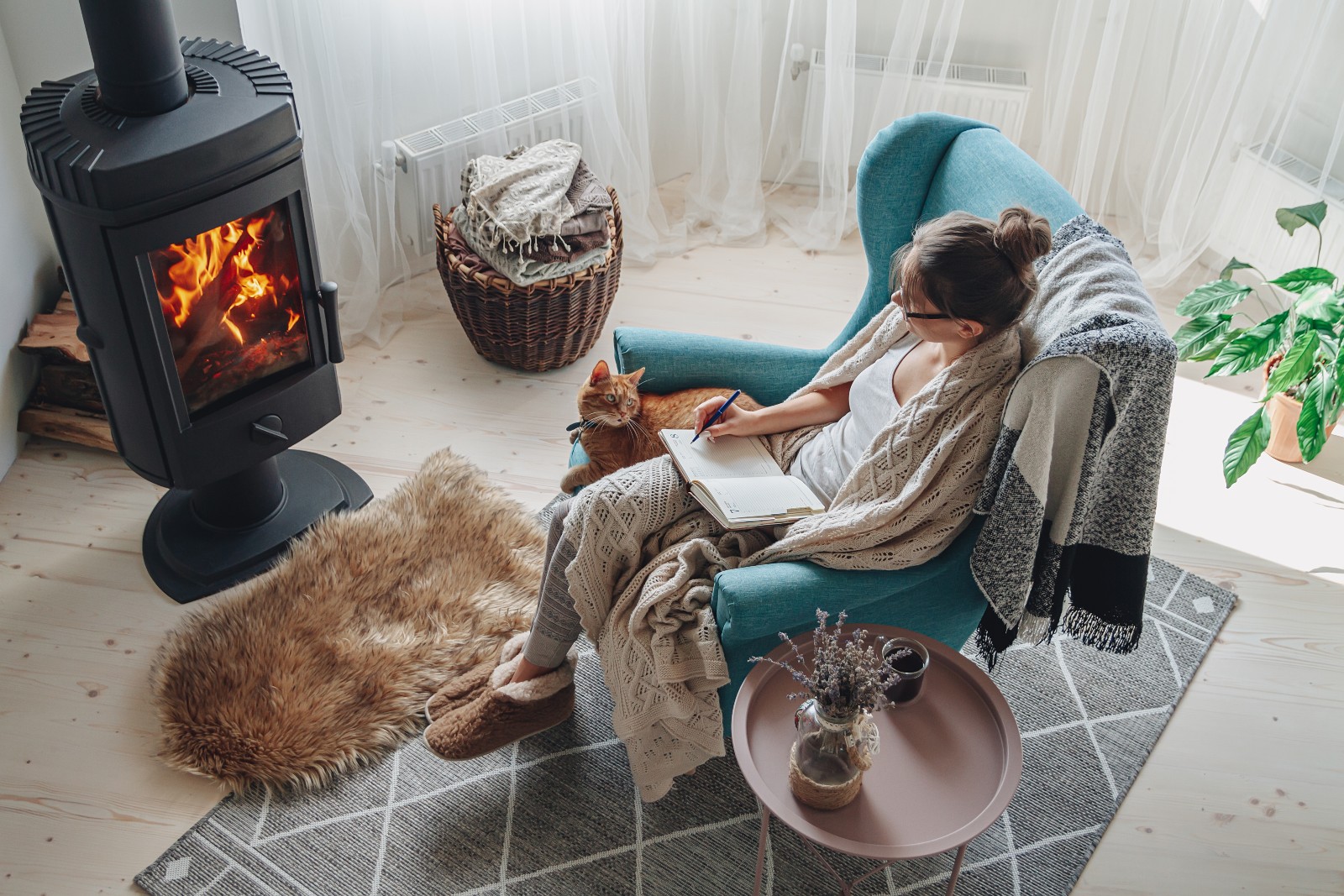 Frau sitzt in einem Sessel vor einem Ofen | Credit: iStock.com/perfectlab