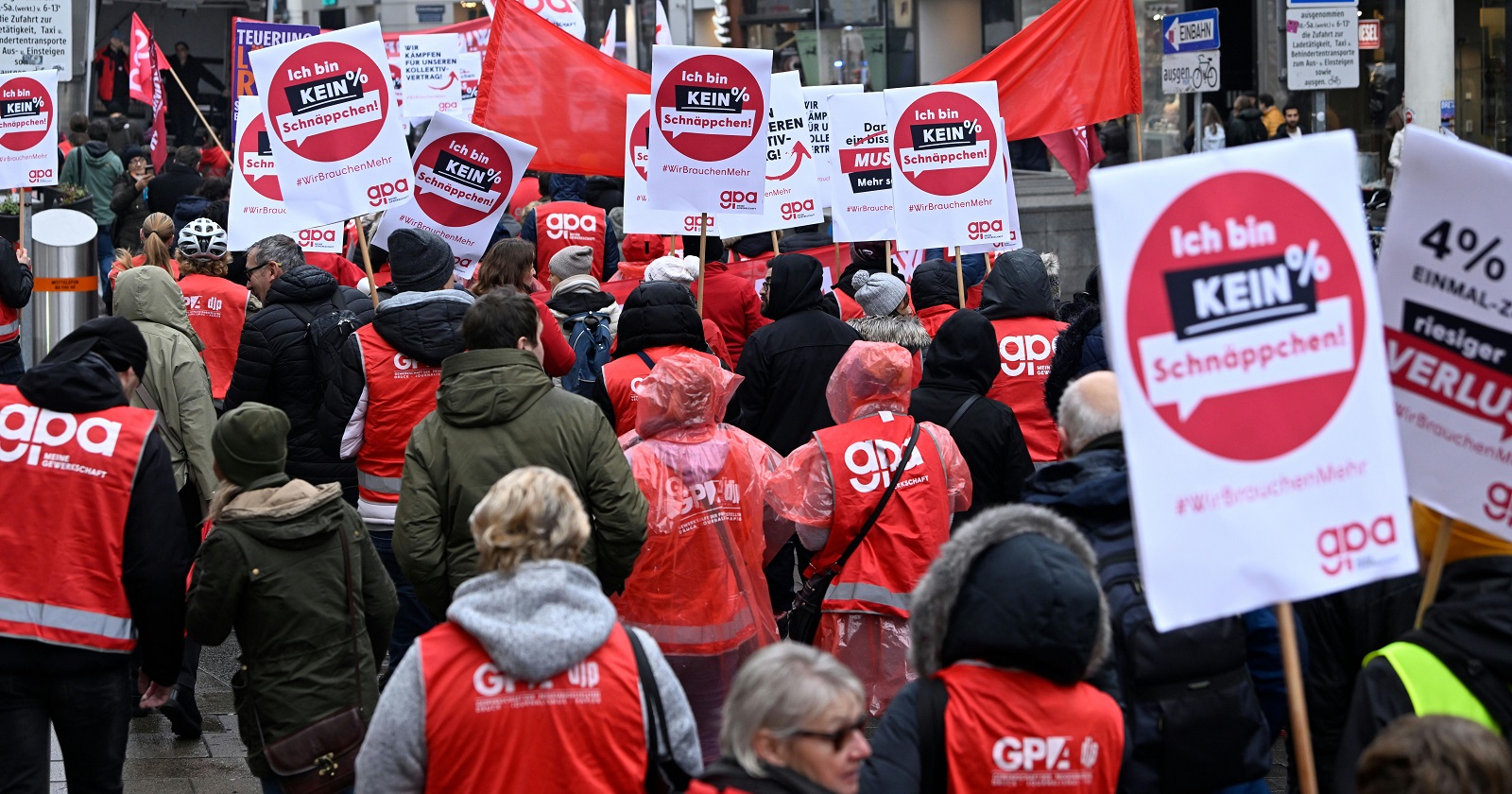 Menschen in roten Westen mit der Aufschrift "GPA" demonstrieren mit Plakaten für ein höheres Gehalt.
