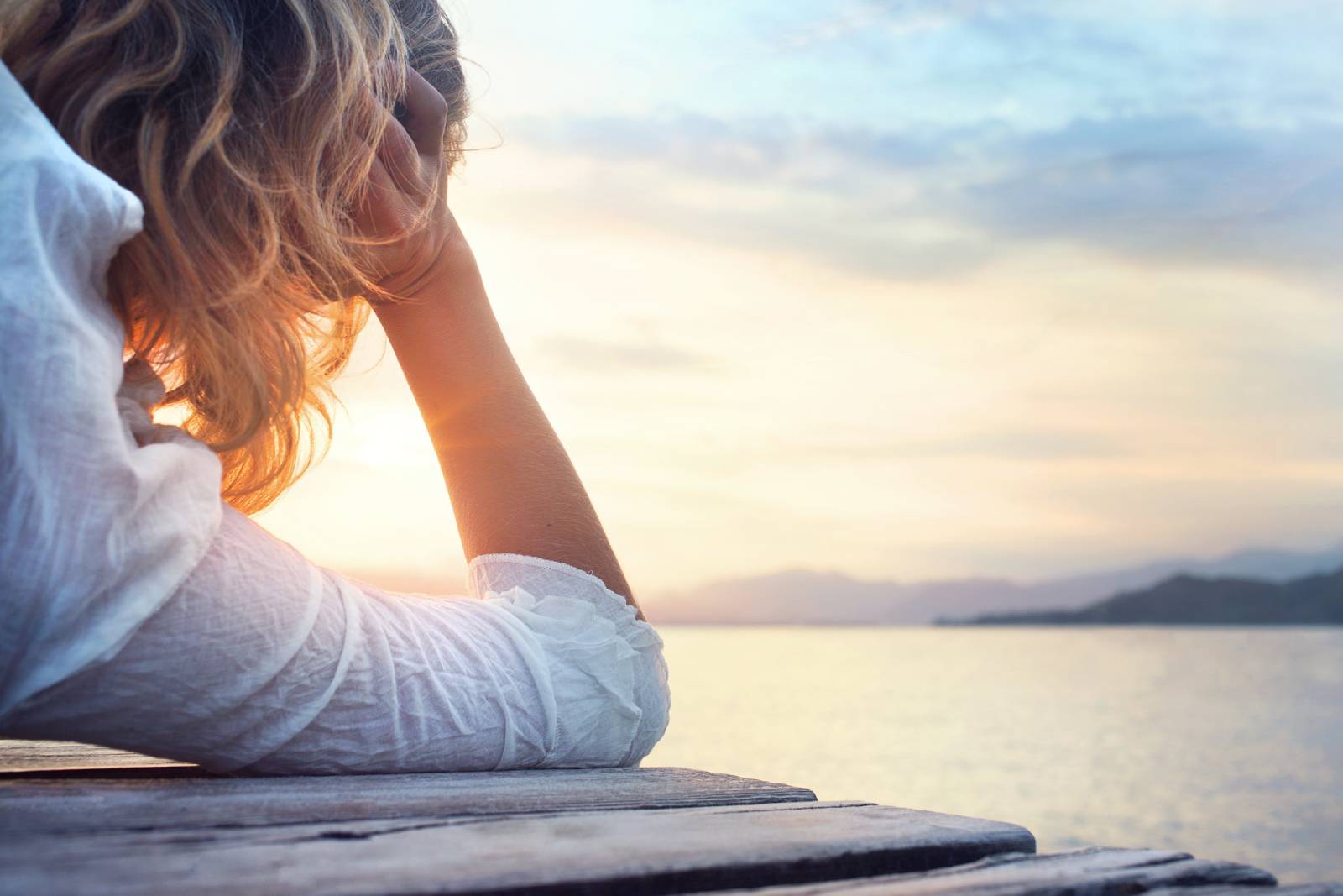 Junge Frau liegt bei Sonnenuntergang auf einem Steg und blickt in die Ferne | Credit: iStock.com/francescoch
