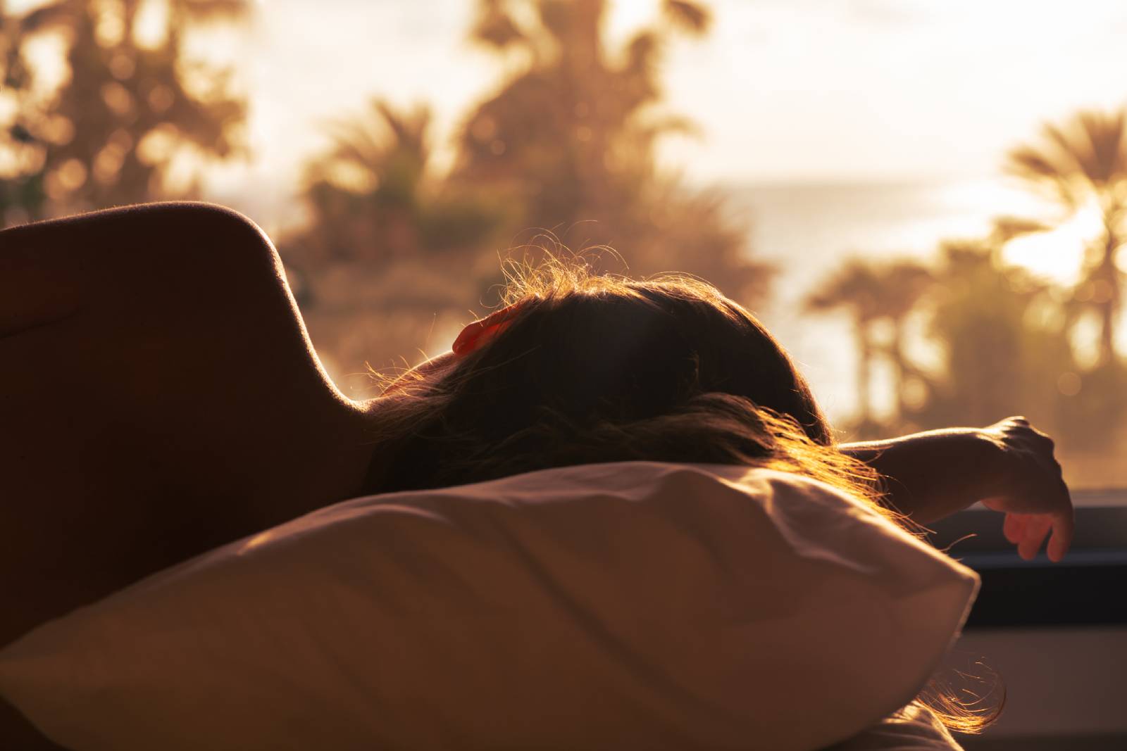 Junge Frau schläft in ihrem Bett bei Sonnenaufgang | Credit: iStock.com/FTiare