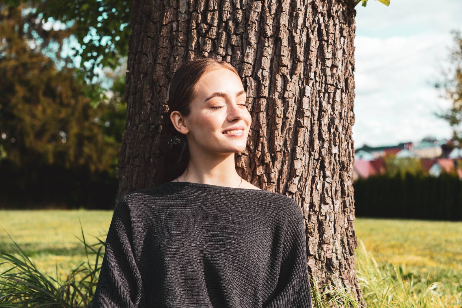Junge Frau entspannt unter einem Baum sitzend die Sonnenstrahlen mit geschlossenen Augen | Credit: iStock.com/Finn Hafemann