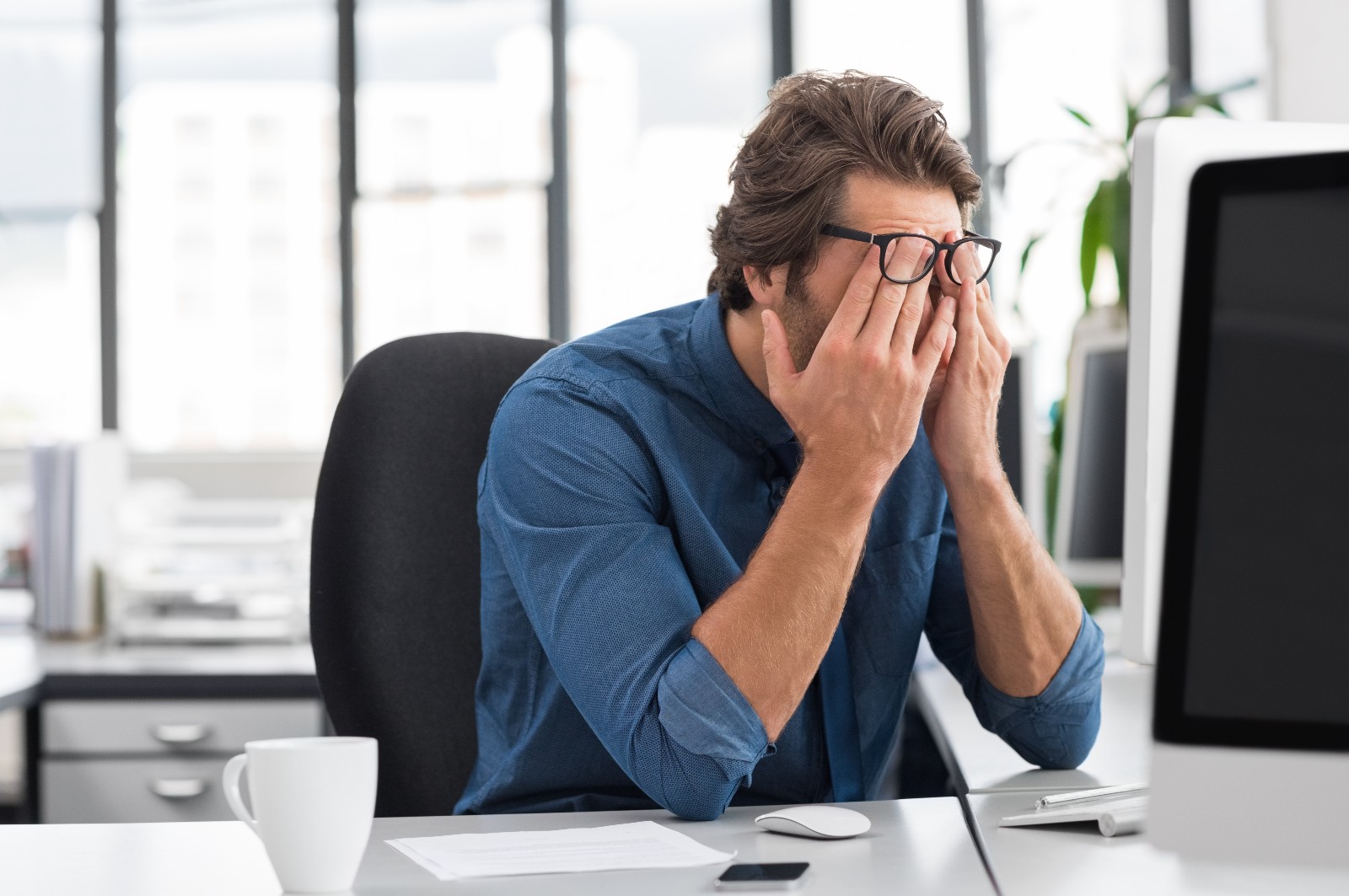 Mann sitzt müde vor seinem Schreibtisch | Credit: iStock.com/Ridofranz