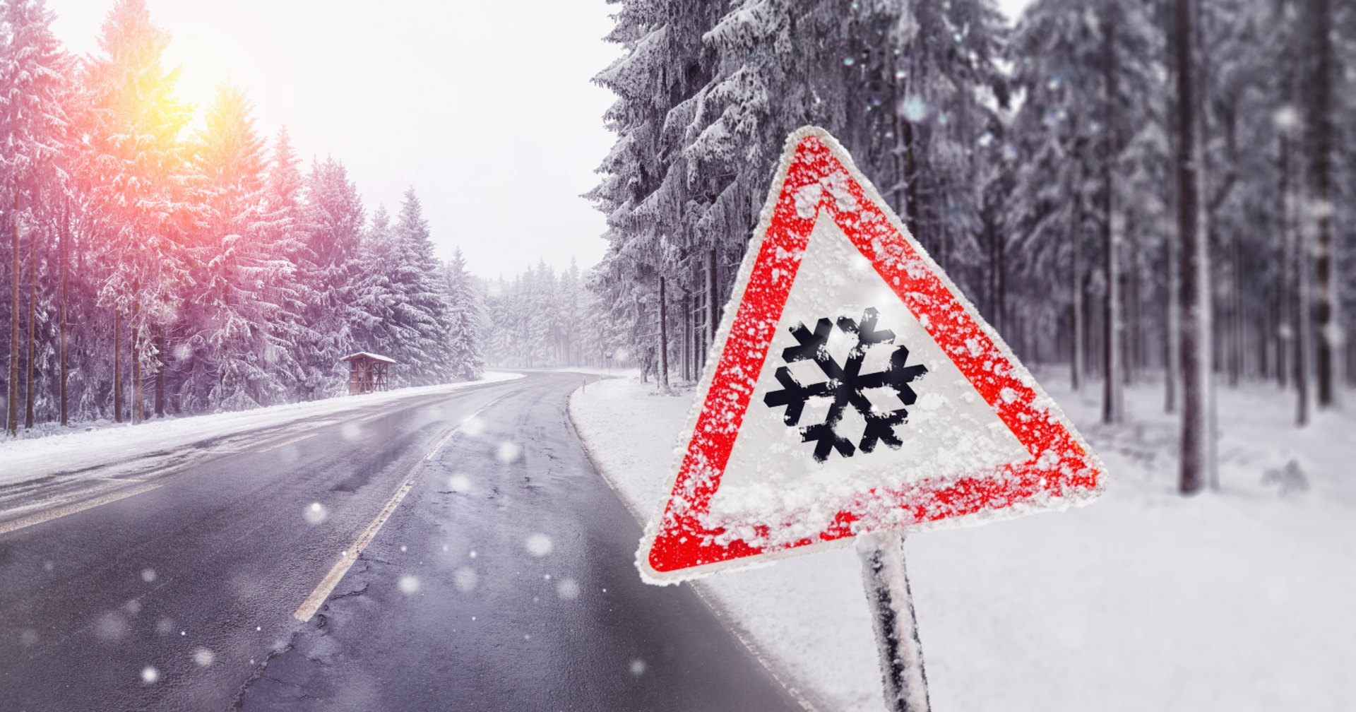 Ein Warnschild, das eine Schneeflocke zeigt, vor einer tiefverschneiten Waldstraße