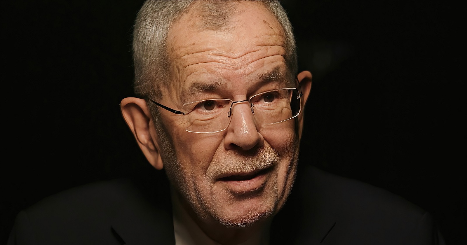 Großaufnahme von Alexander Van der Bellen vor schwarzem Hintergrund.