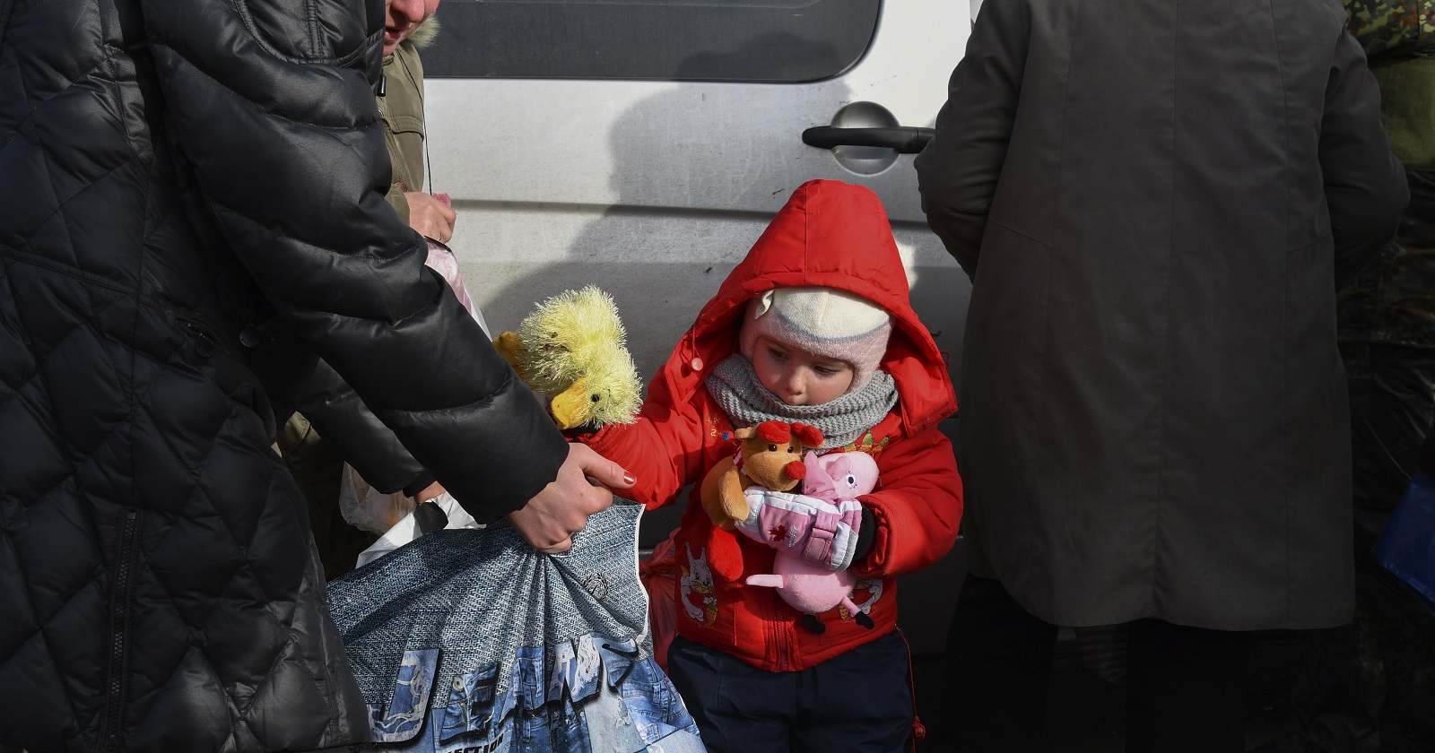Ein Kleinkind in einer roten Kapuzenjacke legt sein Spielzeug in Sackerl.