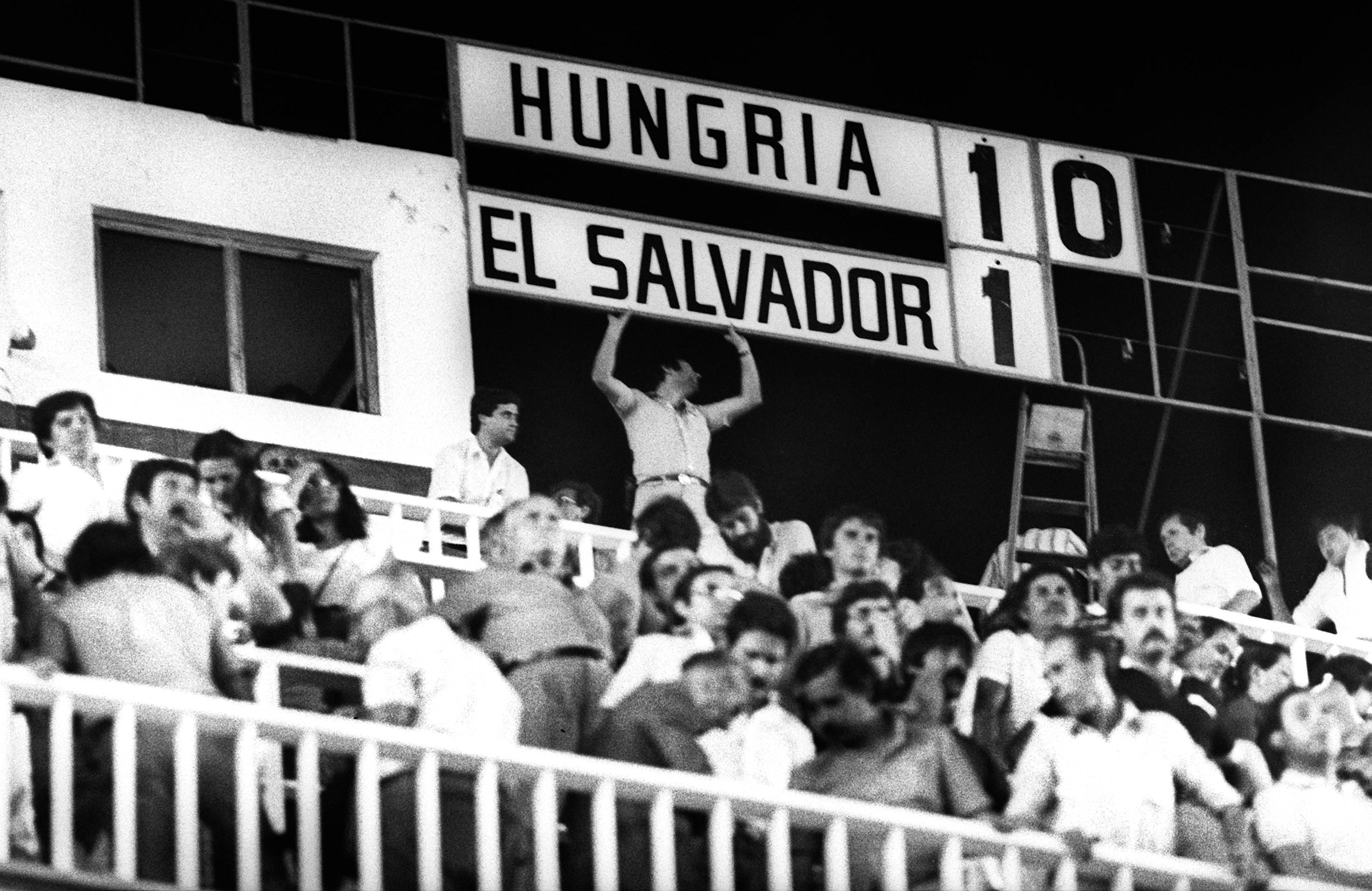 Schwarz-Weiß-Aufnahme der Publikumsränge in der Partie Ungarn - El Salvador. Im Hintergrund ist die Anzeigentafel zu sehen, die das Resultat 10:1 aufweist