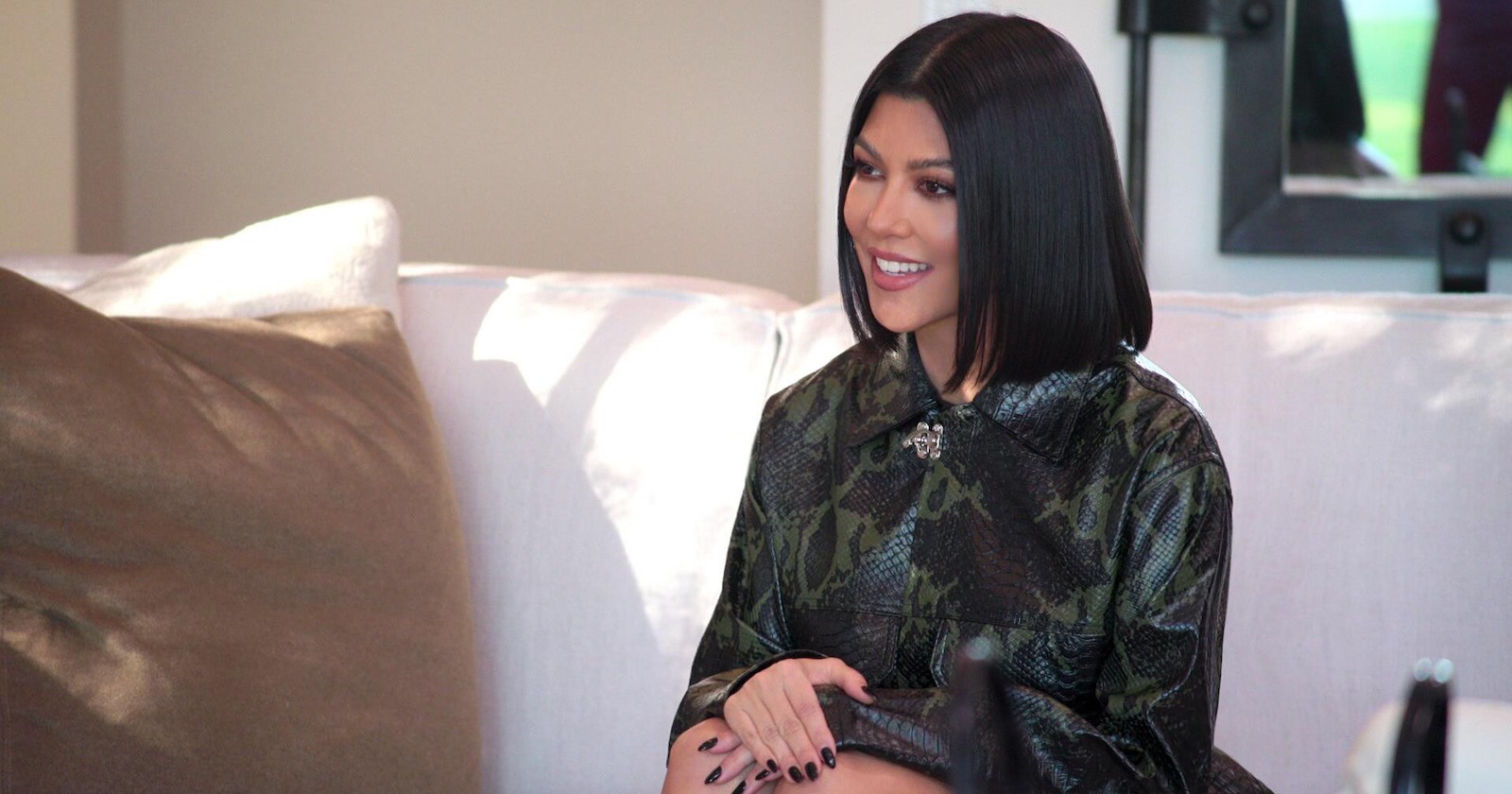 Kourtney Kardashian sitzt auf einer weißen Couch.